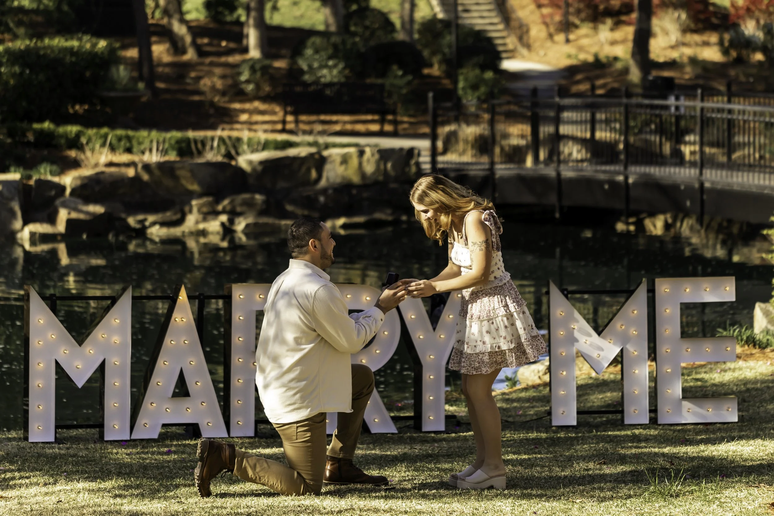 Erick proposing to Faith at Cullman Park in front of 'Marry Me' marquee letters during a surprise engagement