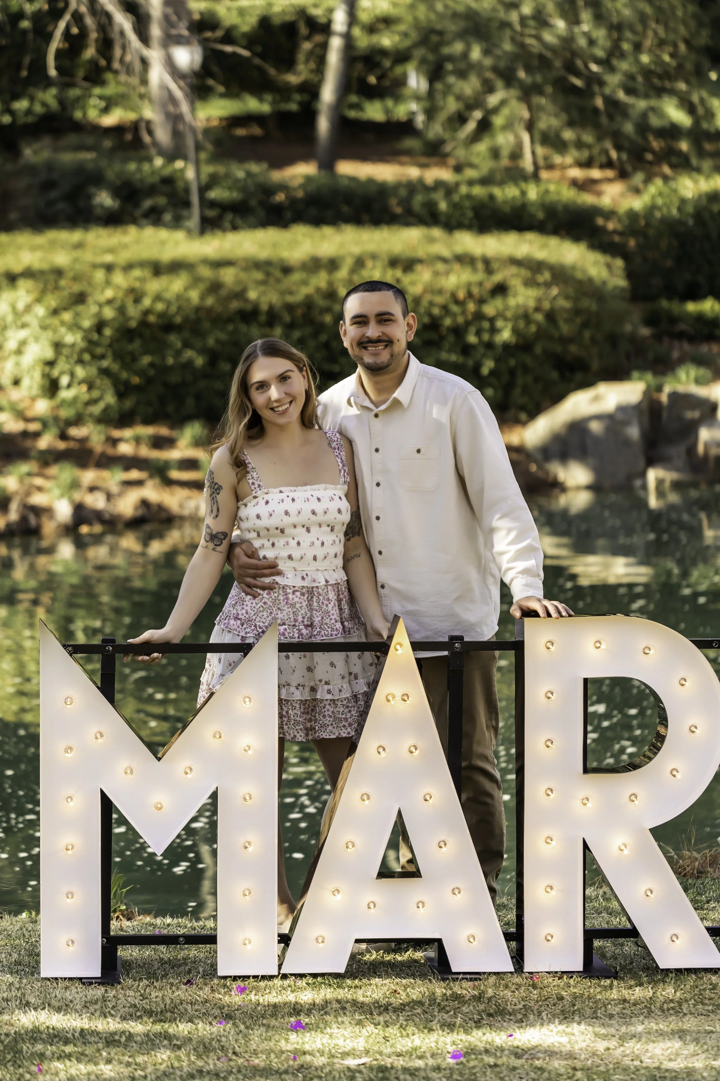 Engagement portraits of Erick and Faith near the lake at Cullman Park, with lush greenery in the background