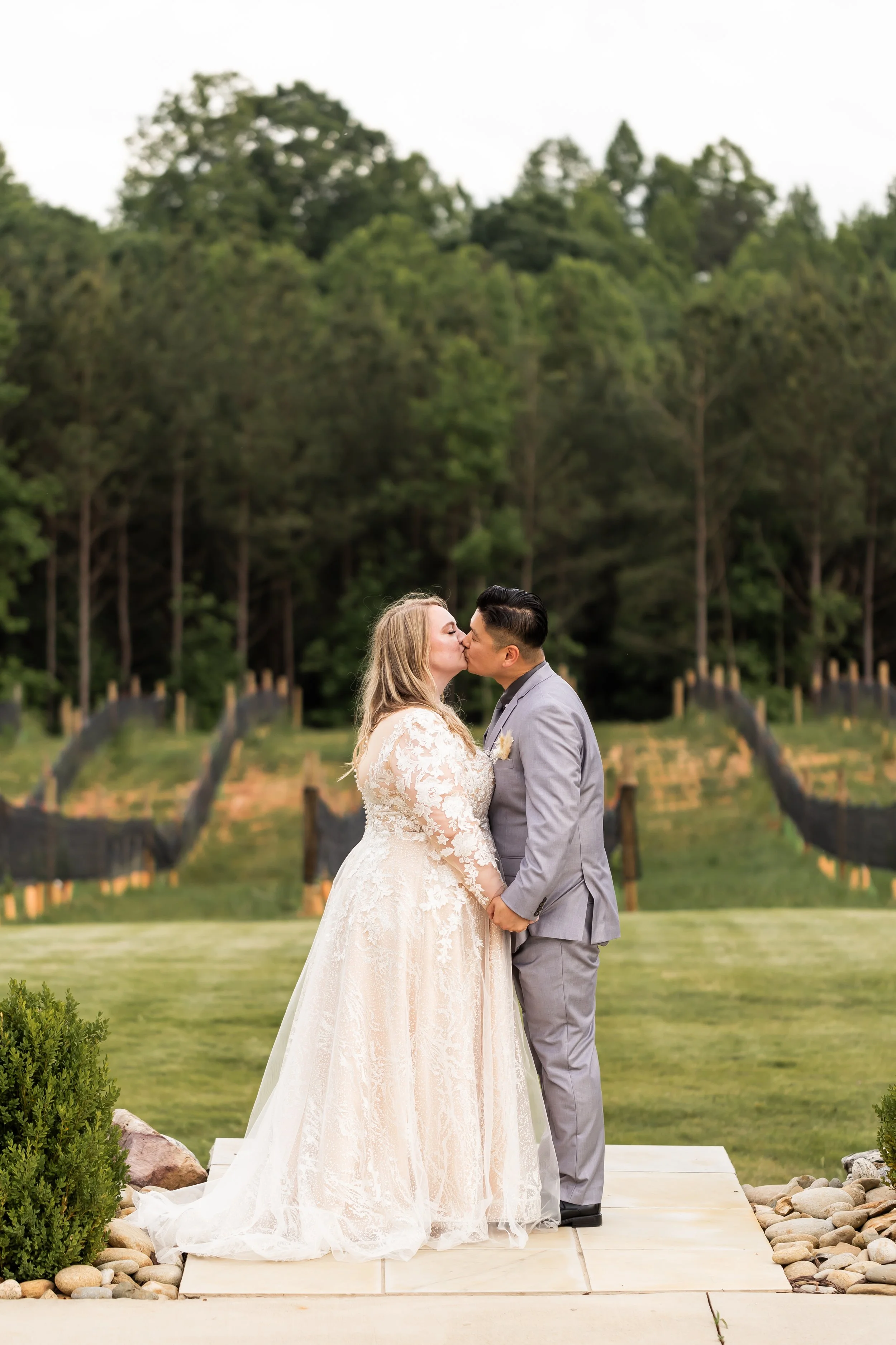 bride and groom kissing with vineyard behind them veronet vineyard nc