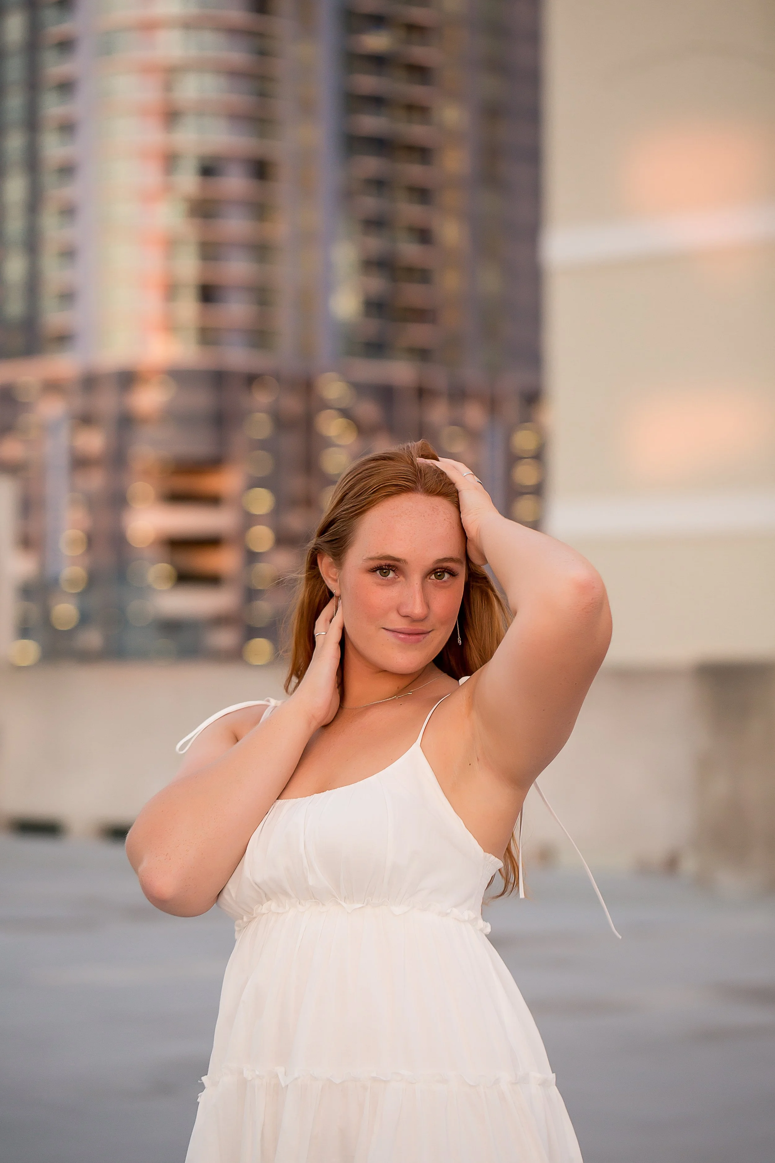 girl with red hair in white dress poses on rooftop in downtown charlotte senior photo shoot