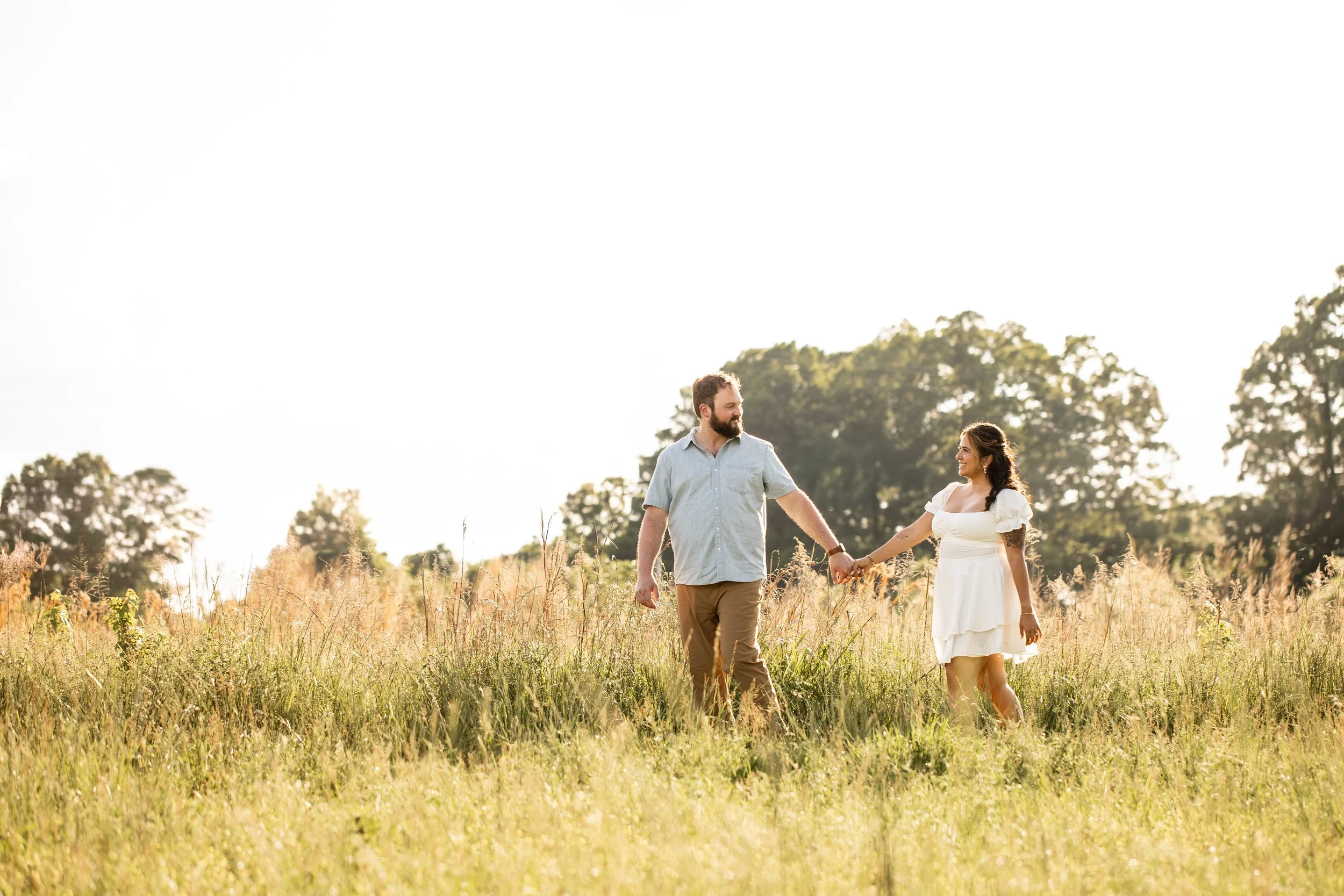 Vanessa and Alex walking hand in hand through golden grass fields at Clark's Creek Nature Preserve during their engagement session