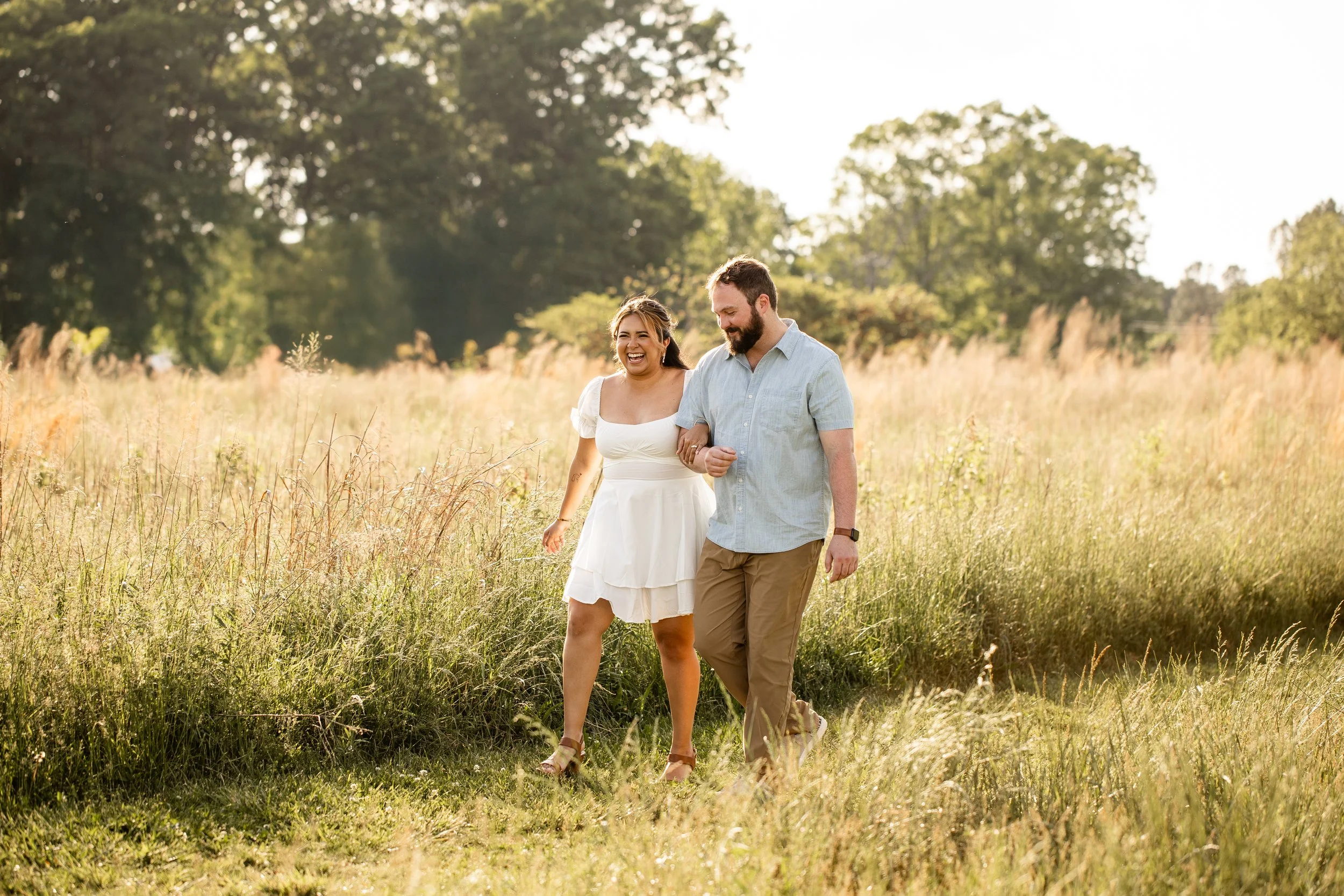 Vanessa and Alex walking hand in hand through golden grass fields at Clark's Creek Nature Preserve during their engagement session