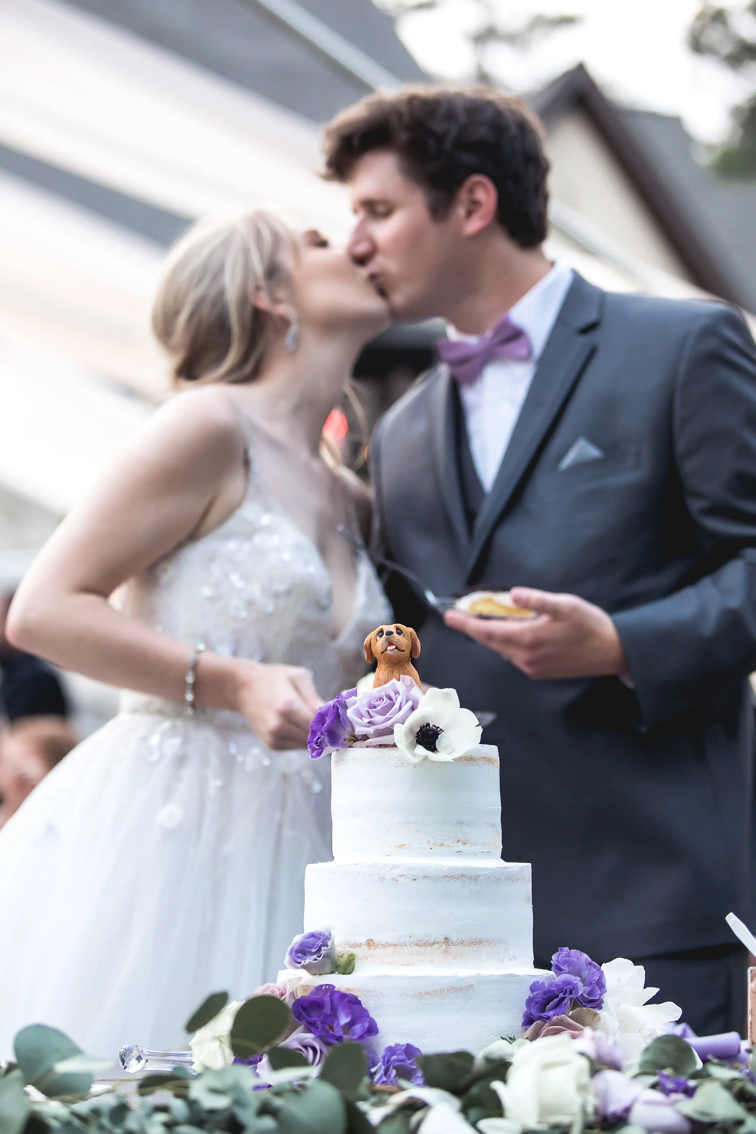 couple kiss and cuts cake at wedding cake has dog topper