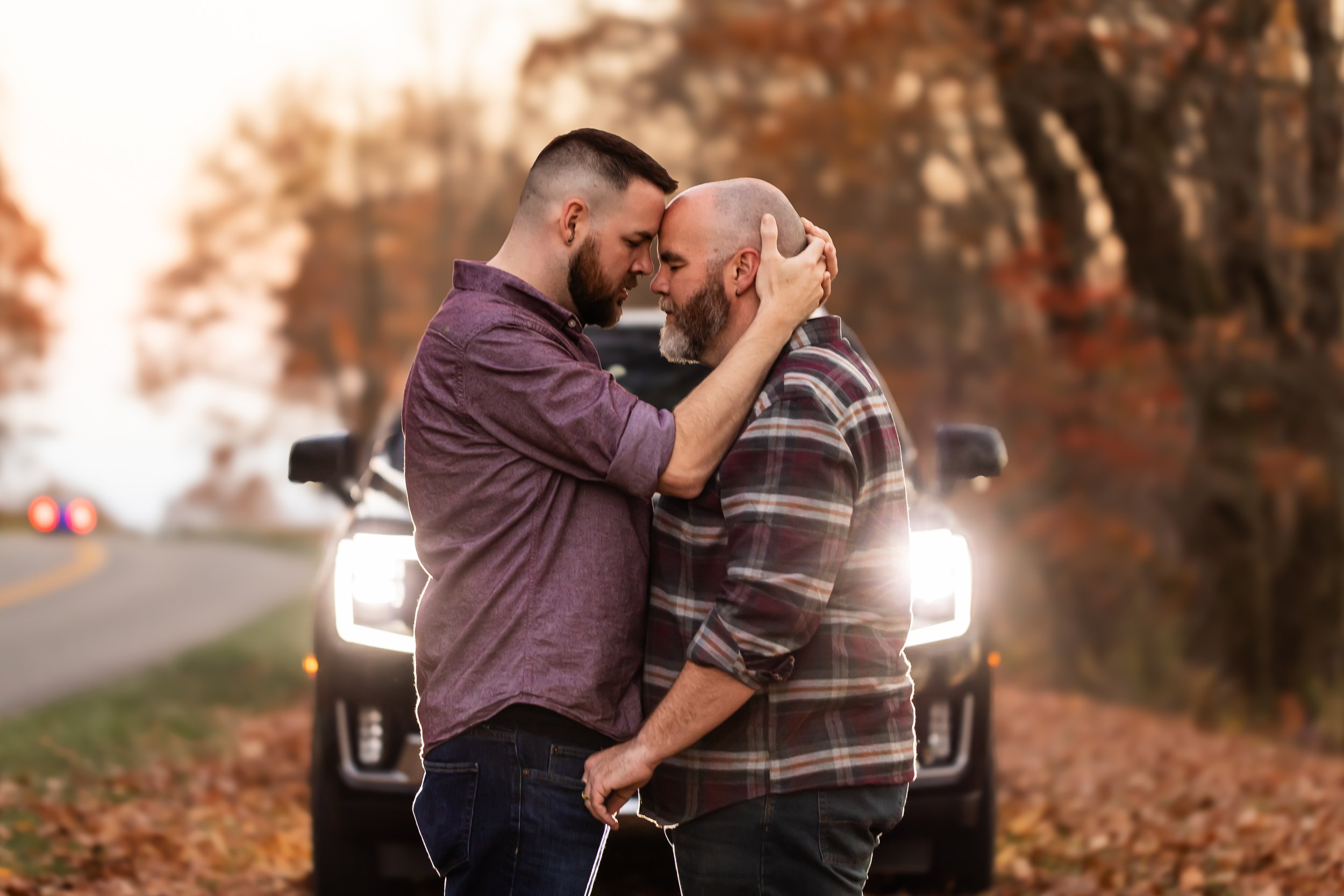 gay men engaged photo sessoin standing in front of headlights in the mountains dusk