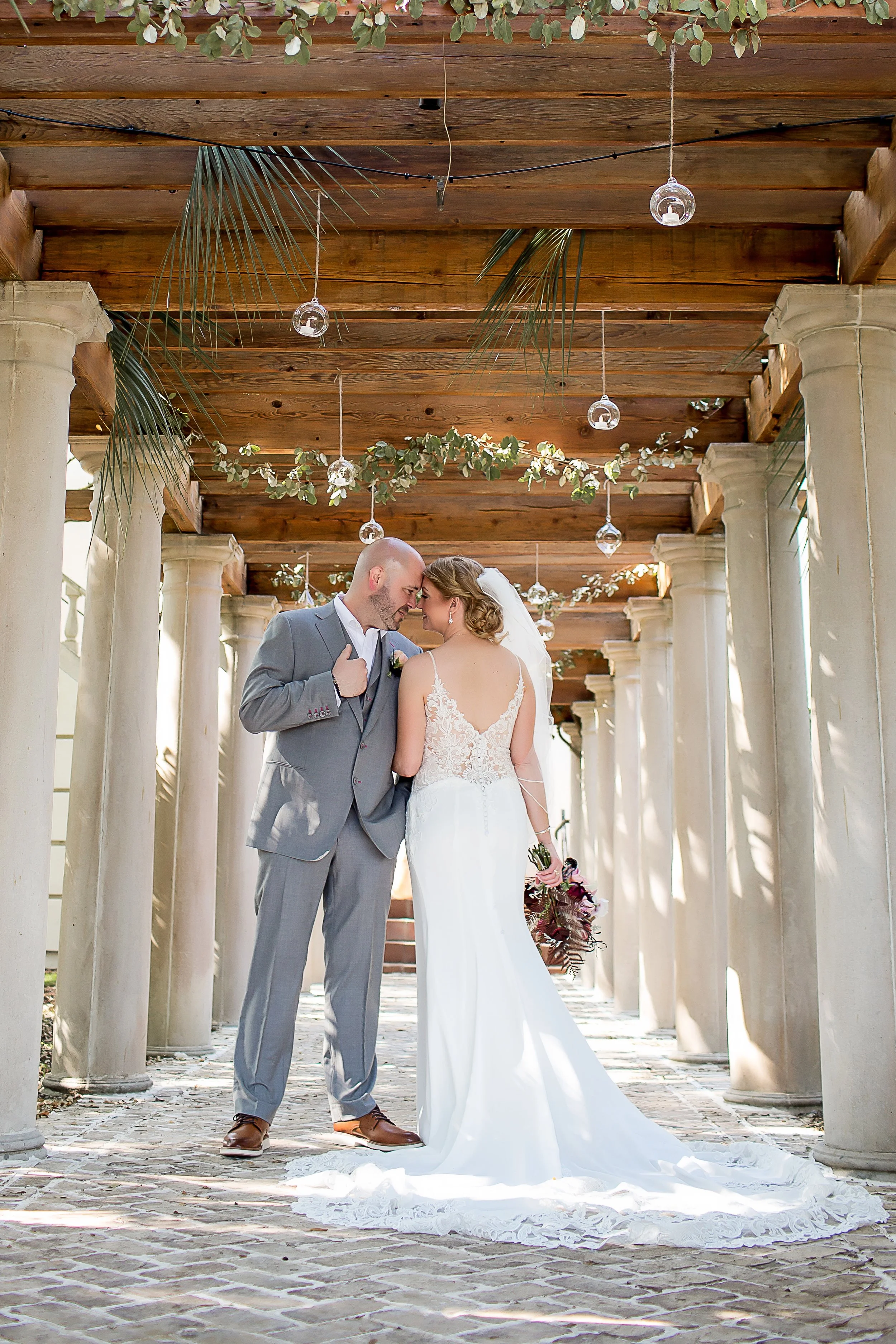 Bride and groom stand forehead to forehead under arbor lit with twinkle lights in charleston mansion