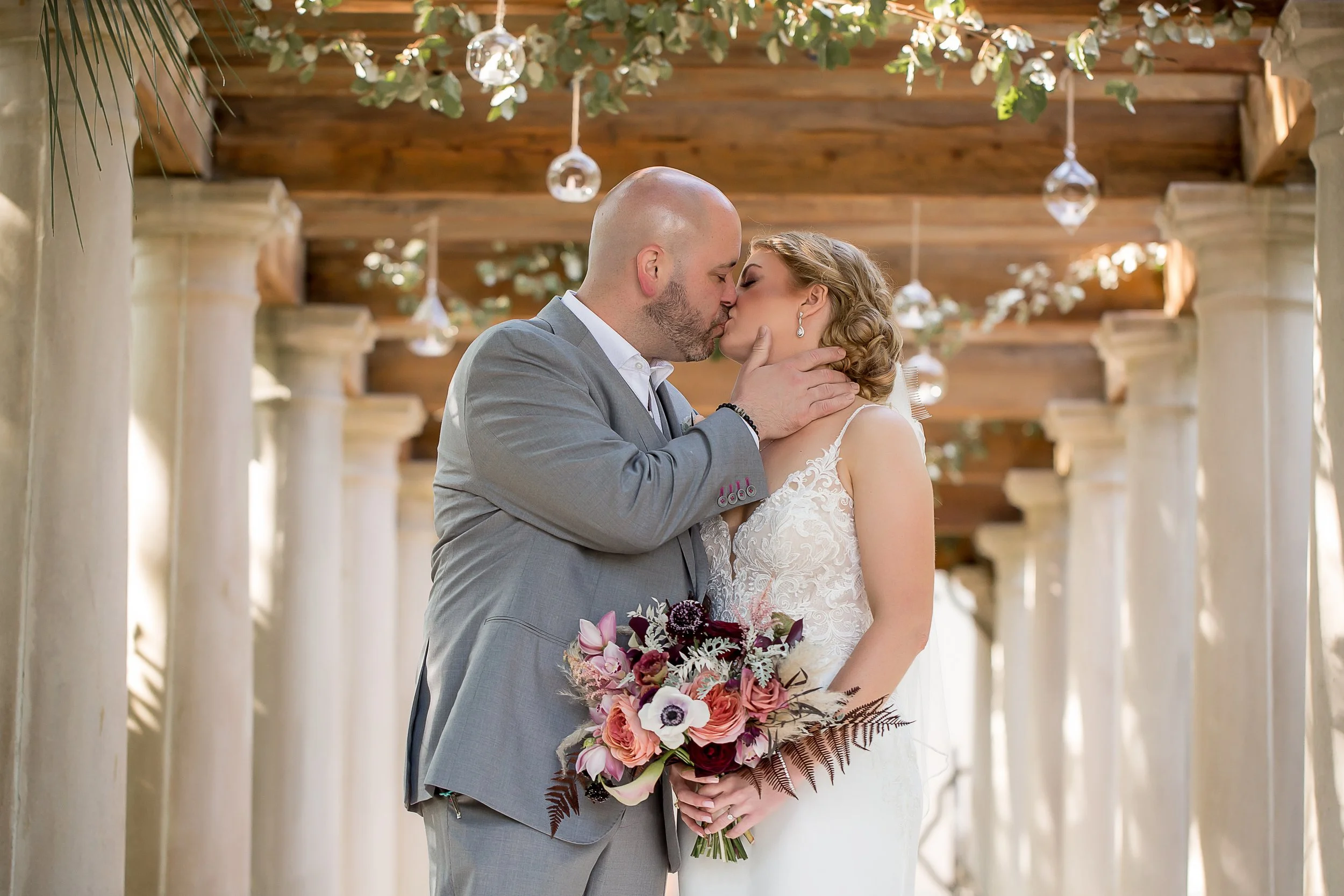 charleston destination wedding bride and groom kissing under arbor with sophisticated floral bouquet