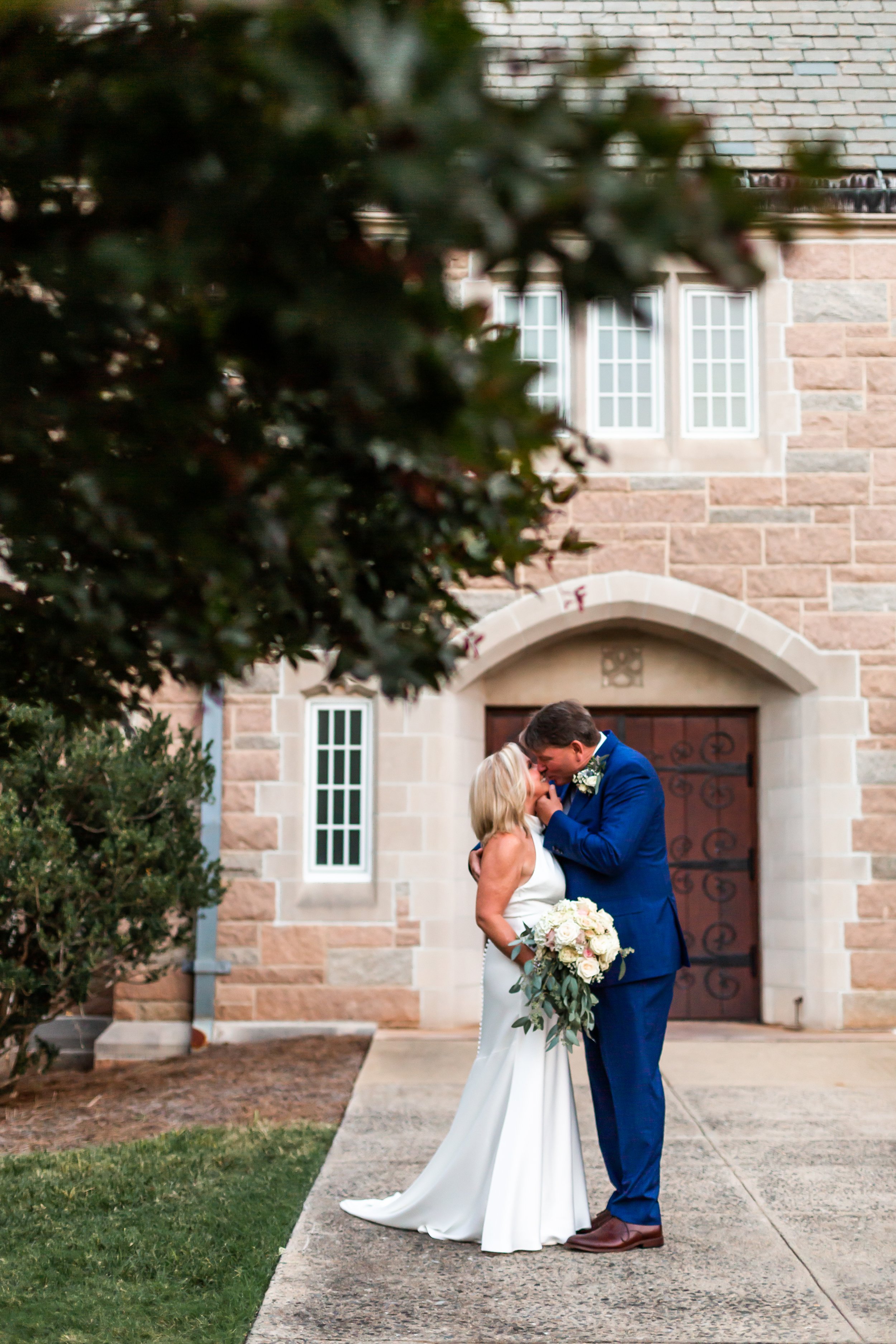 vertical portrait older bride and groom kissing under a large tree in front of church charlotte nc