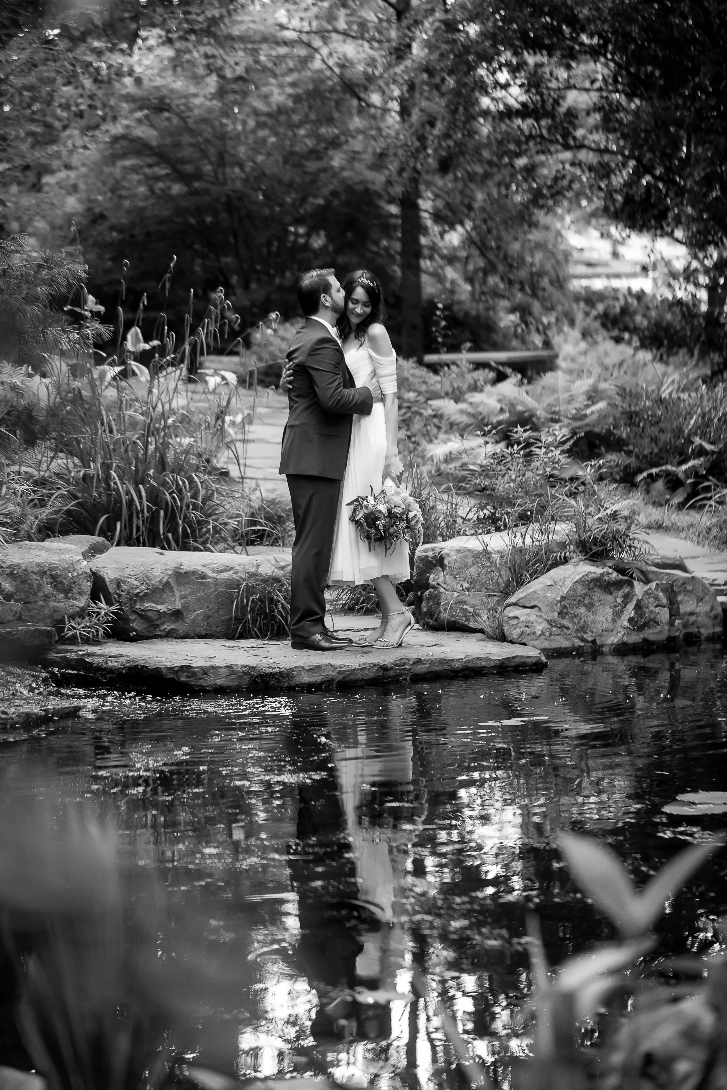 black and white image of married couple and their reflection in a pond at uncc botanical gardens afternoon elopement