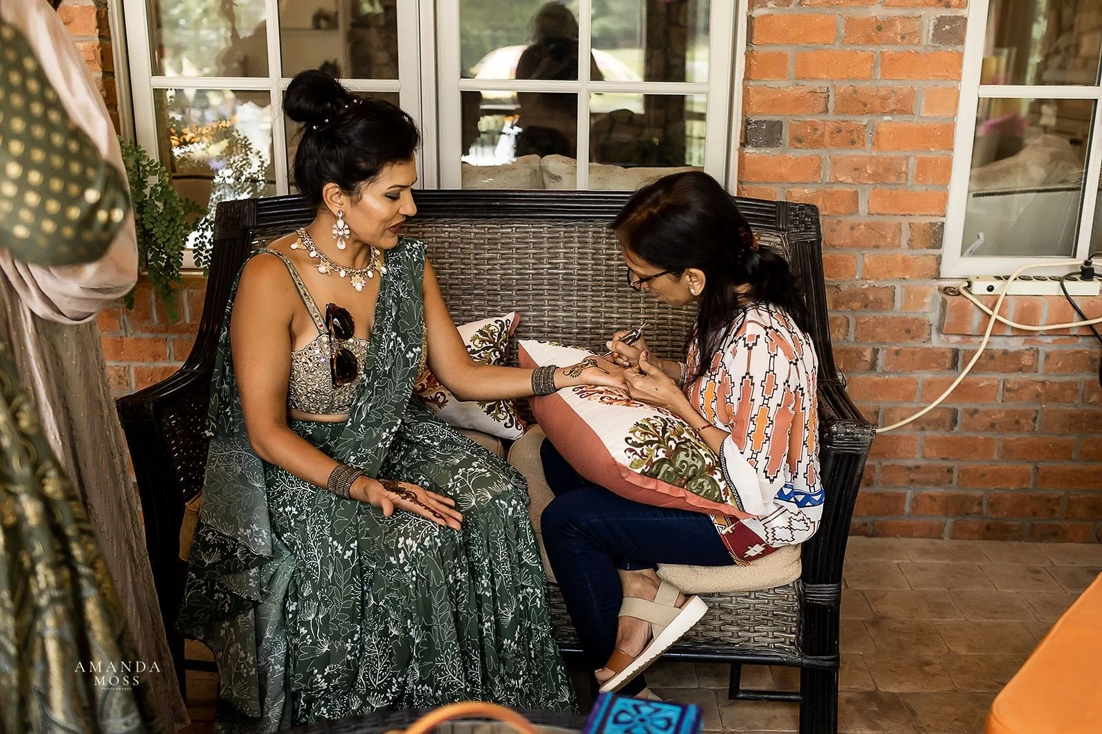  woman applies henna to another womans hands at a mendhi ceremony 