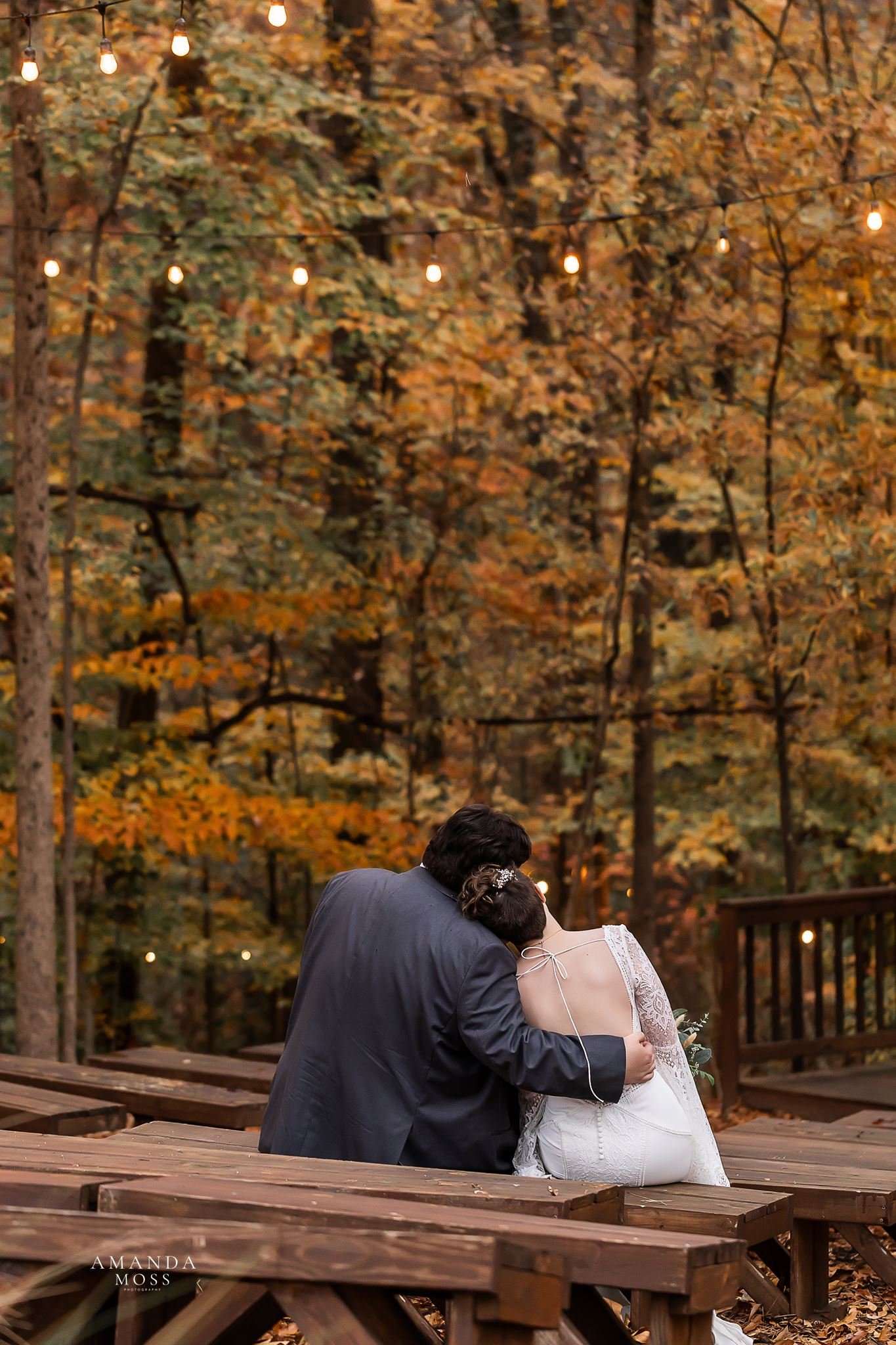 photo of bride and groom sitting on wooden pews and looking in the distance at their outdoor fall wedding at bansen farms