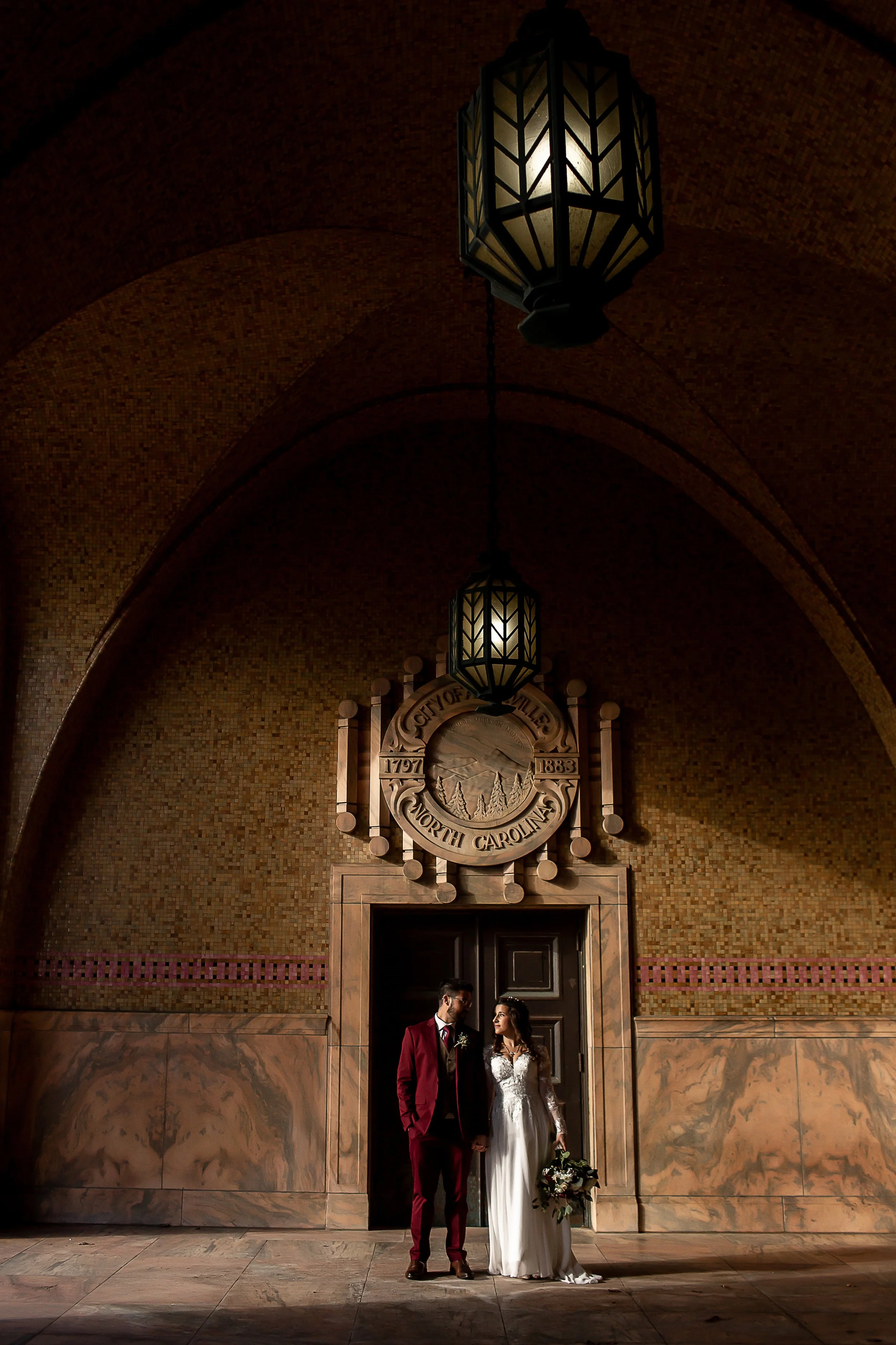bride and groom stand under large architecture of asheville courthouse