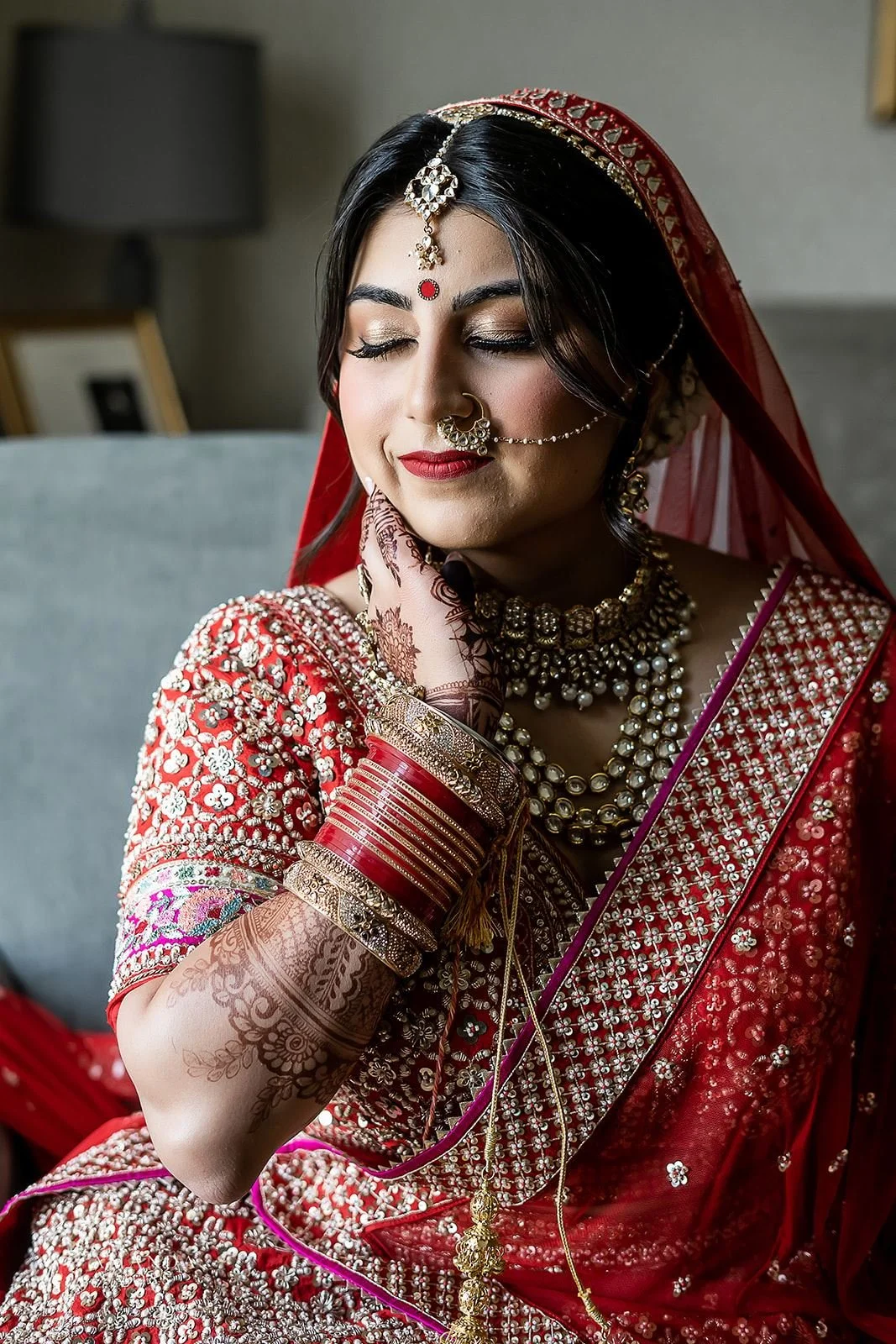 portrait of indian bride in red and gold attire with her eyes close and hand resting gently on her neck
