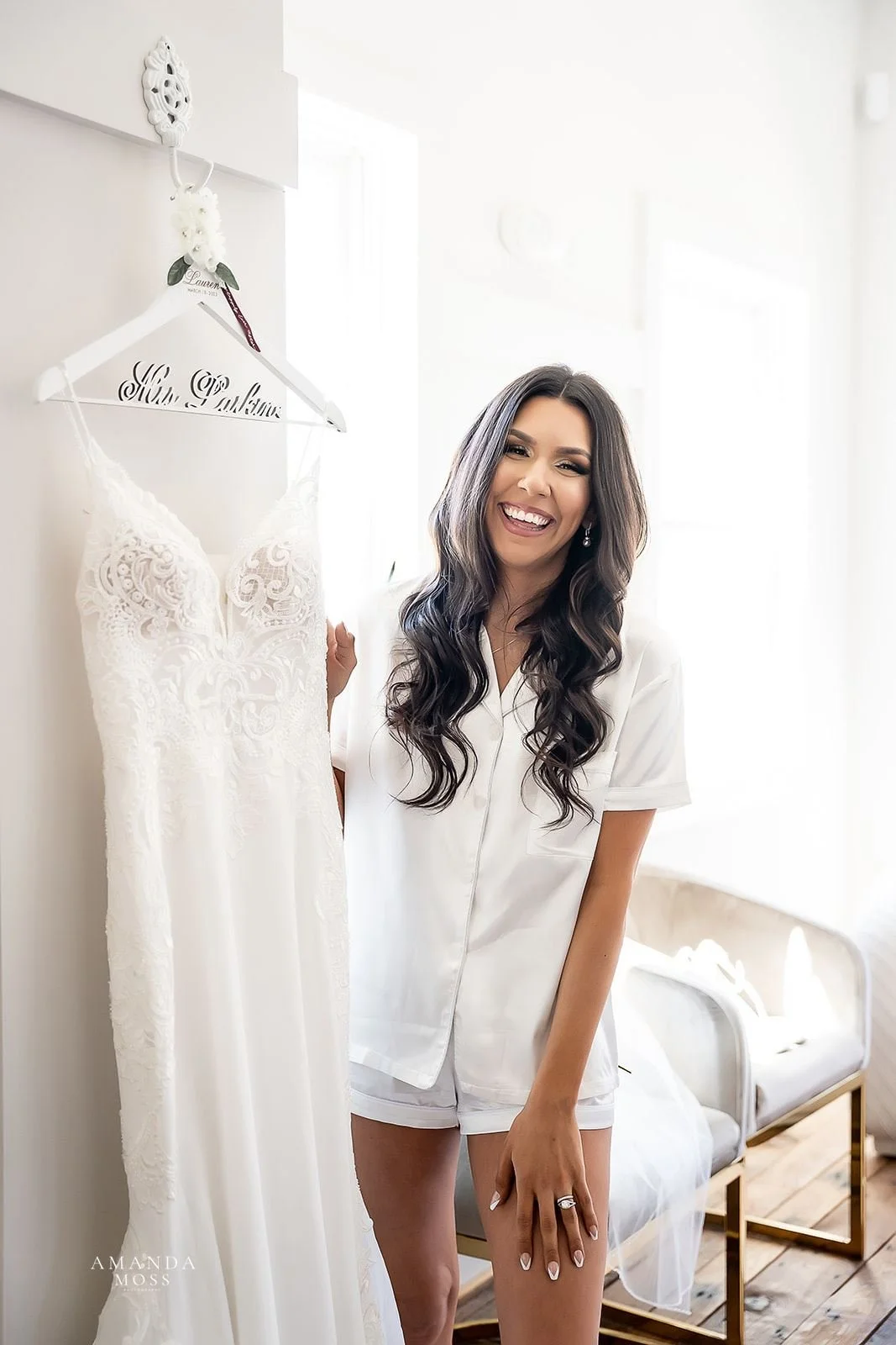 bride with long brown hair smiles while holding her wedding dress before she gets into it on her wedding day