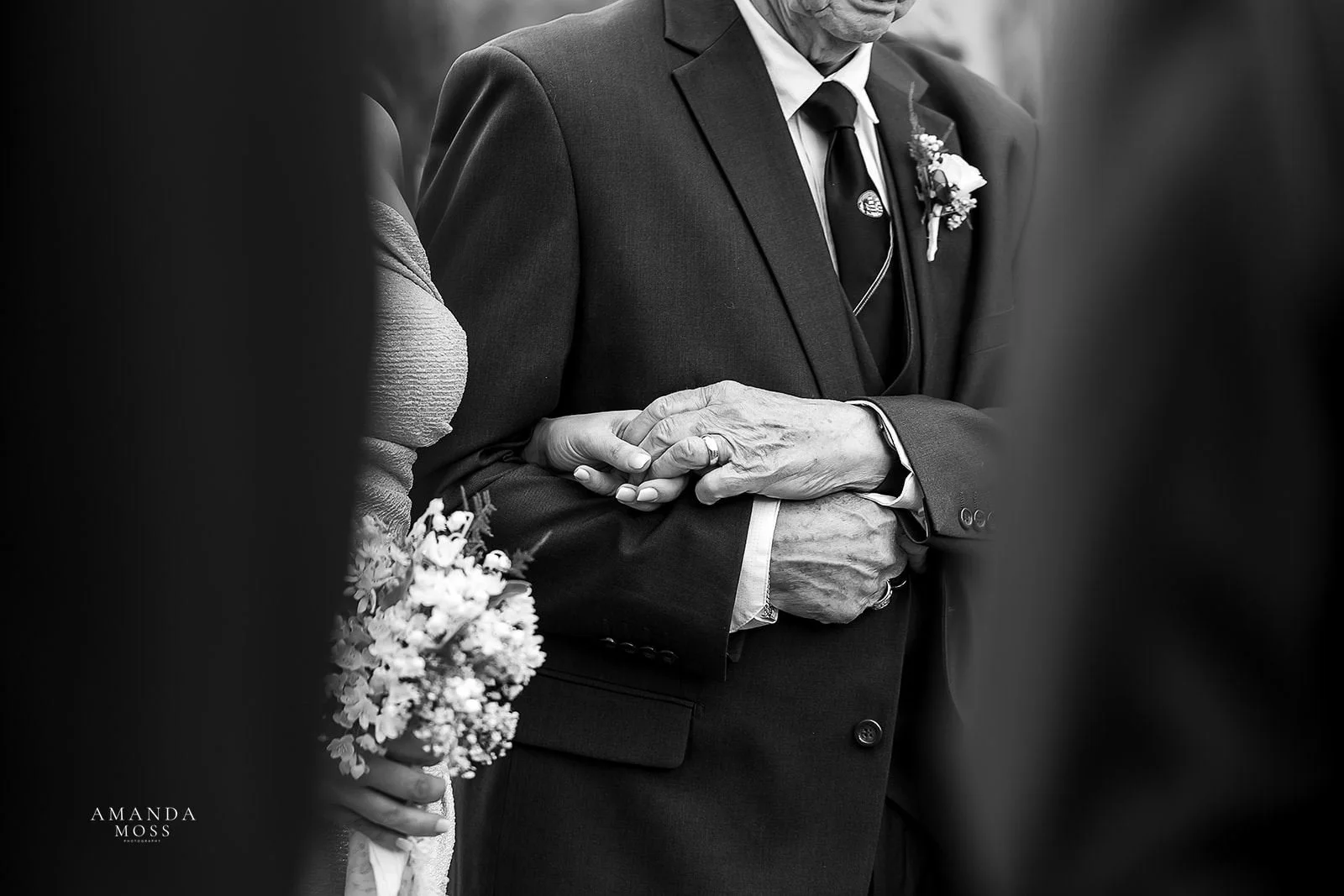 black and white photo of bride and her dad holding hands while he walks her down the aisle at stowe conservancy botanical garden in belmont nc