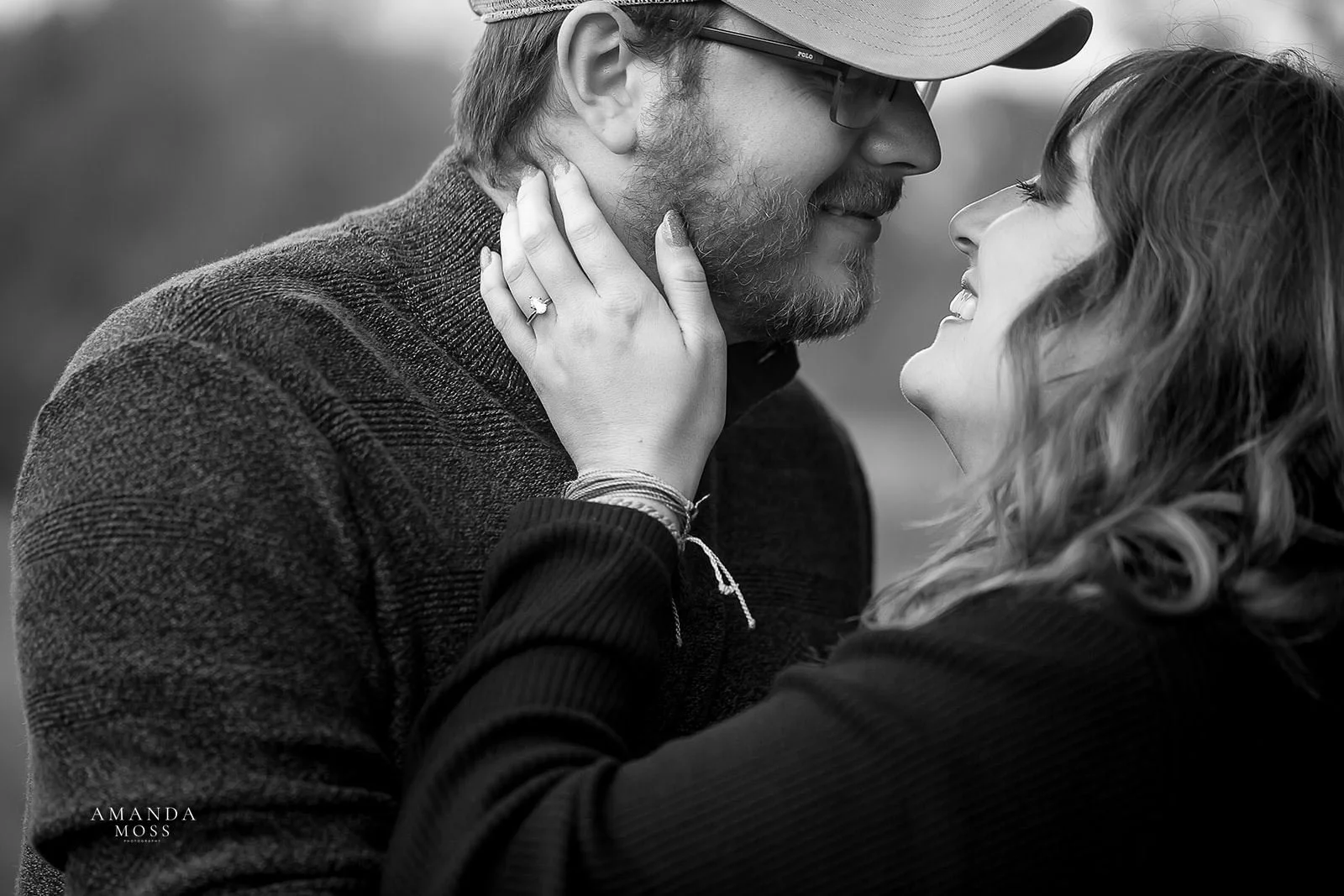 black and white photo close up of man and woman about to kiss while smiling. her hand is on his face and she is wearing an engagement ring