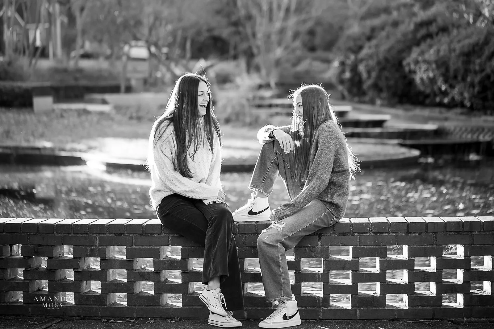 two sisters sit on a brick wall and laugh with each other black and white photo