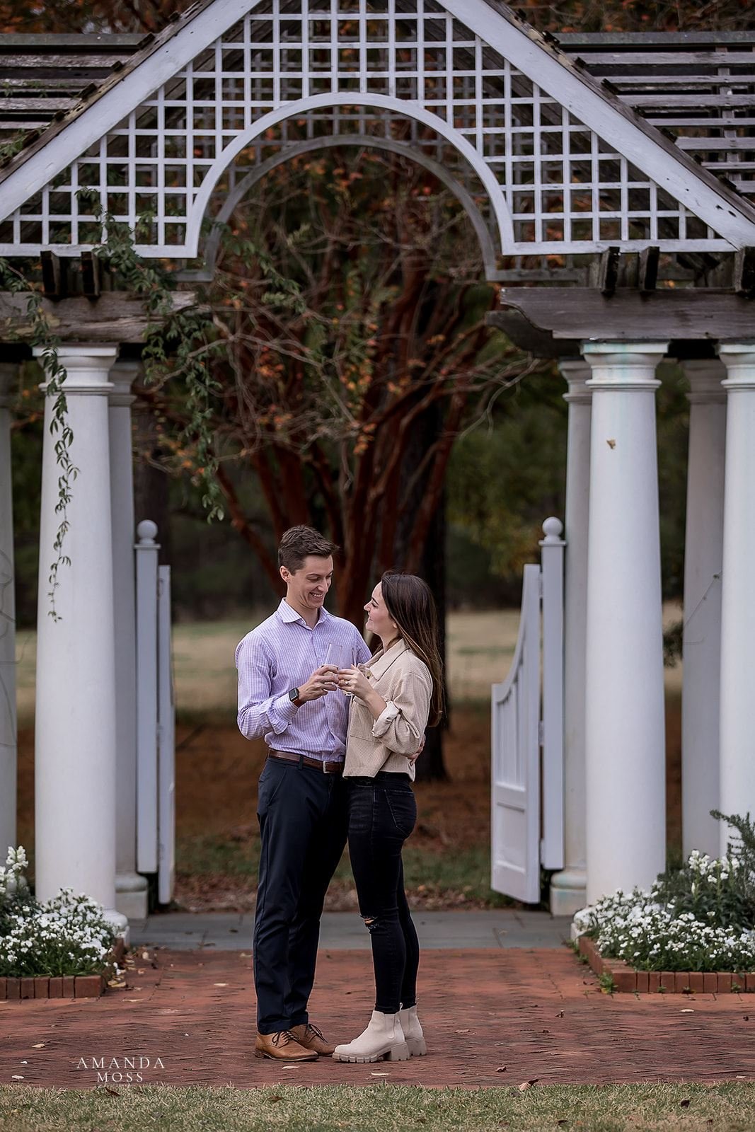 couple toasts with champagne under white garden arbor at daniel stowe botanical garden after proposal