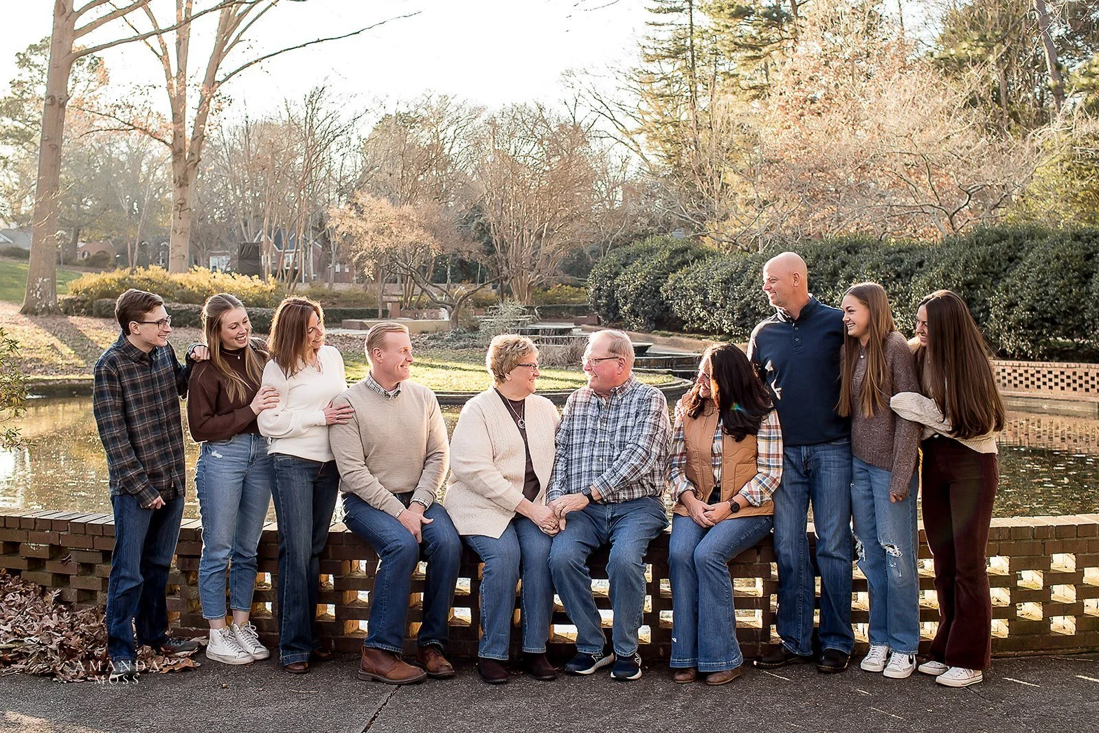 extended family portrait with grandparents parents and children sitting on brick wall in front of a pond
