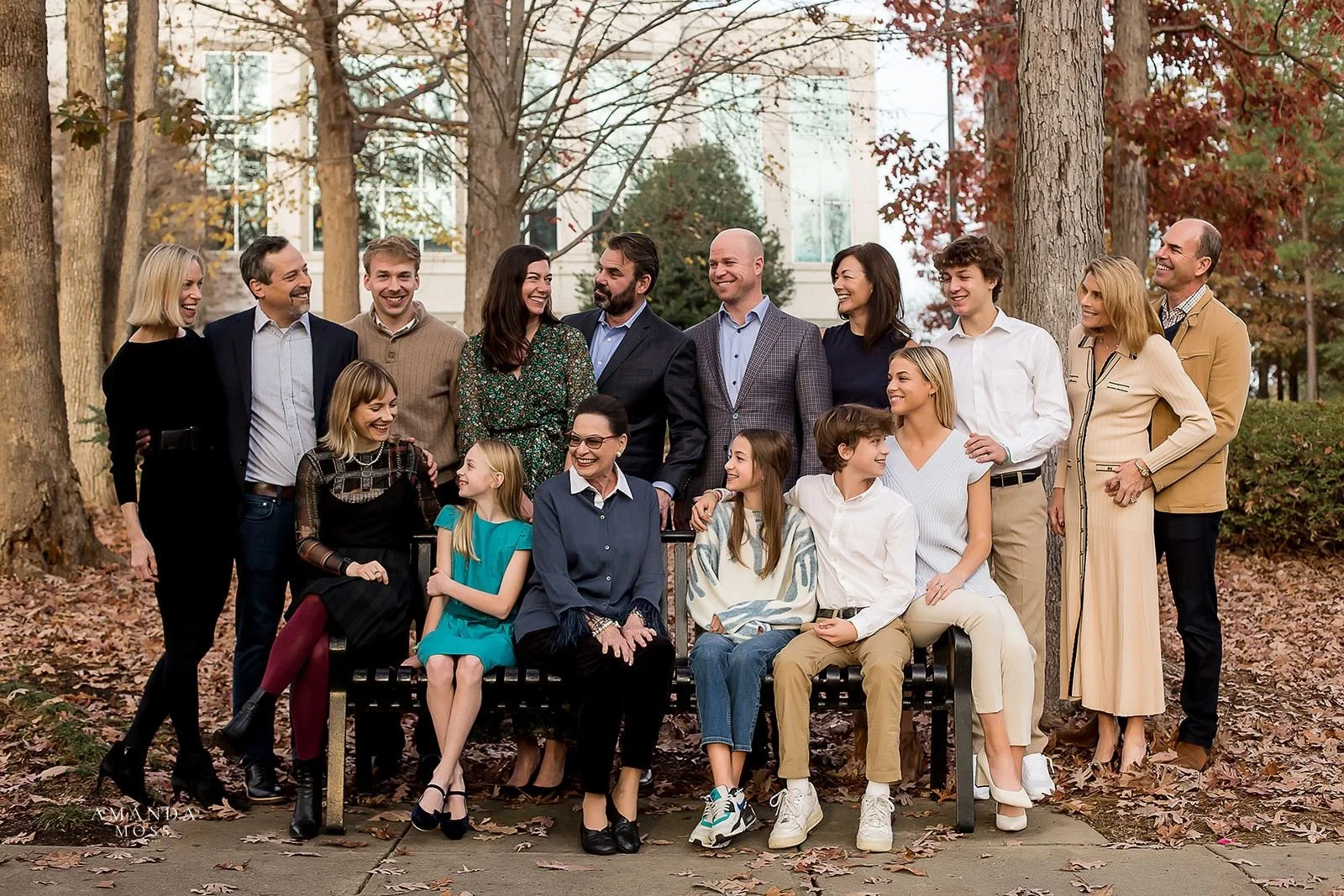 extended family photo with lots of people all looking at each other and smiling at a park in the fall