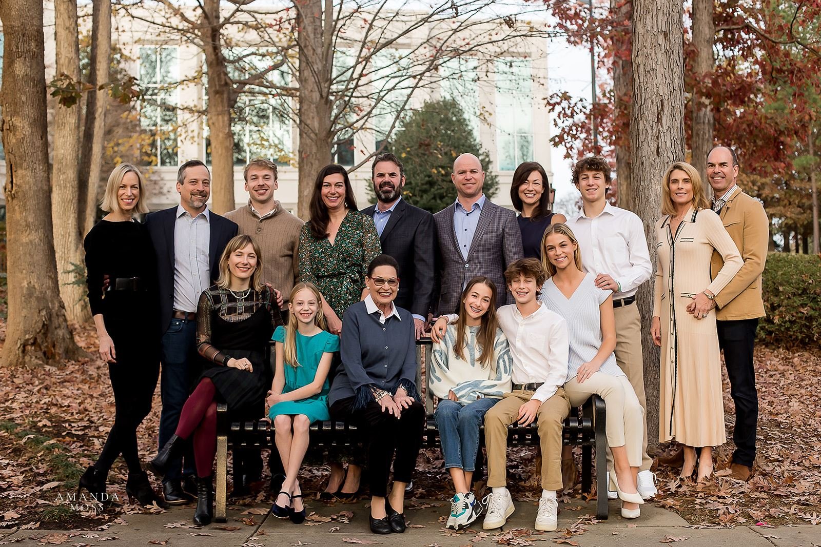 large extended family gathers for photo on park bench in the fall
