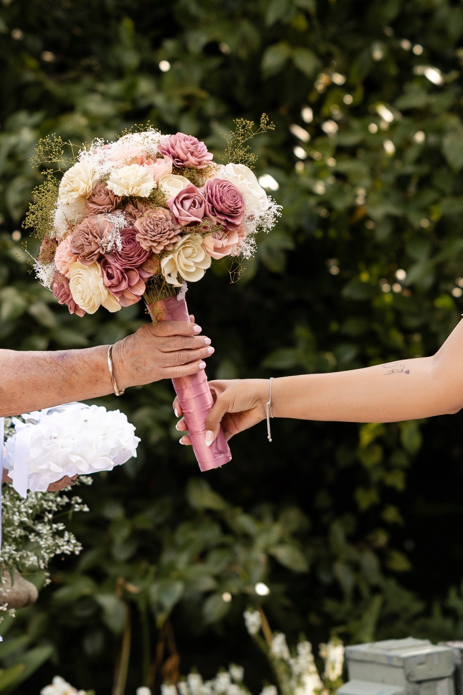 mothers hand reaches out to take bouquet from bride's hand at outdoor wedding ceremony