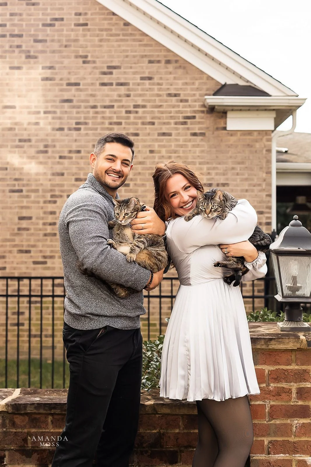 couple poses with their gray tabby cats on charlotte patio for at home family photo session