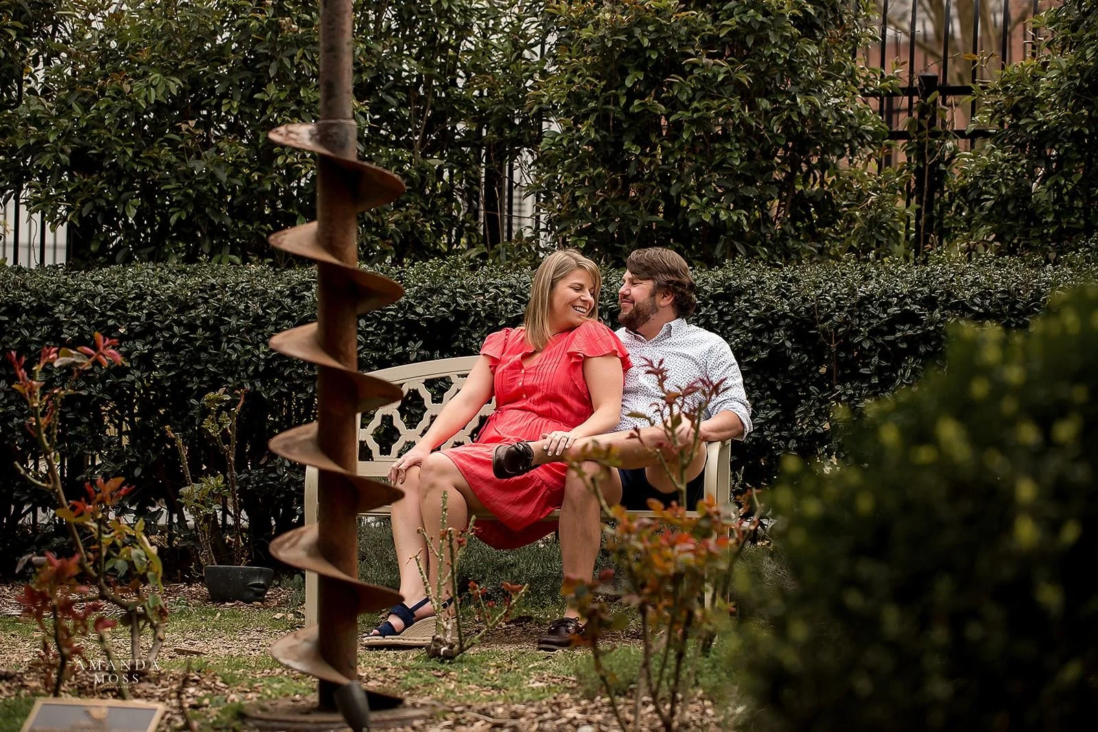 couple sits together on bench and smiles at each other during engagement session at rosies wine bar charlotte nc