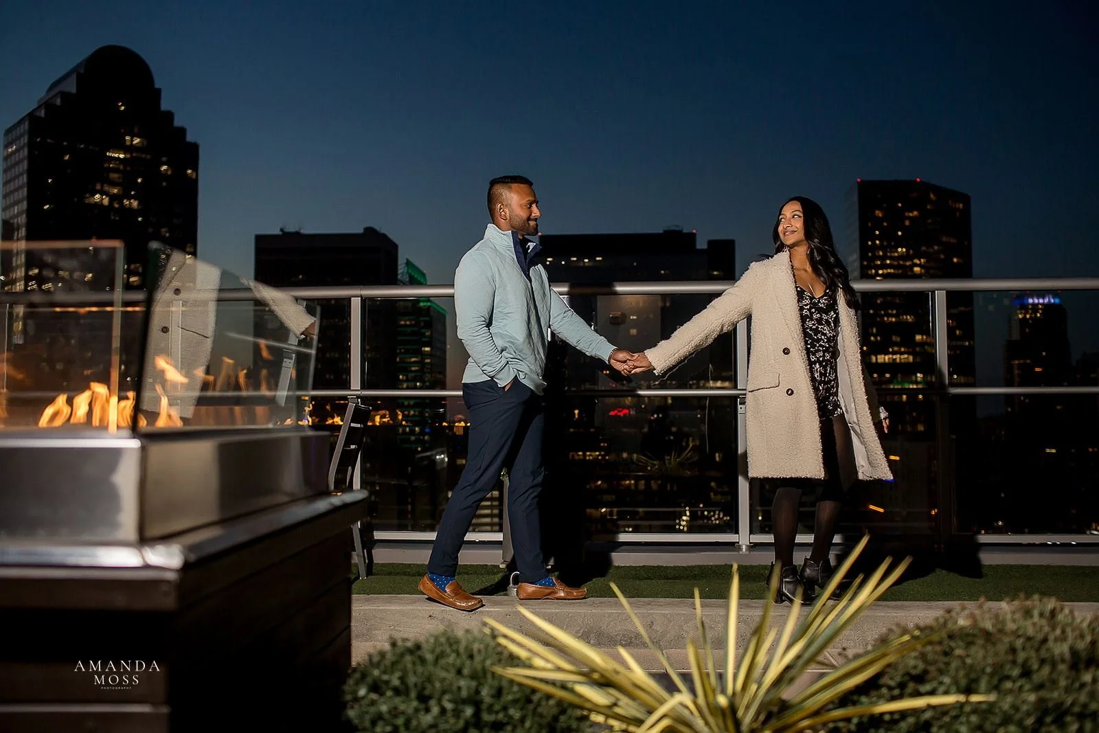woman leads man on a walk across the patio of fahrenheit rooftop with the charlotte skyline behind them