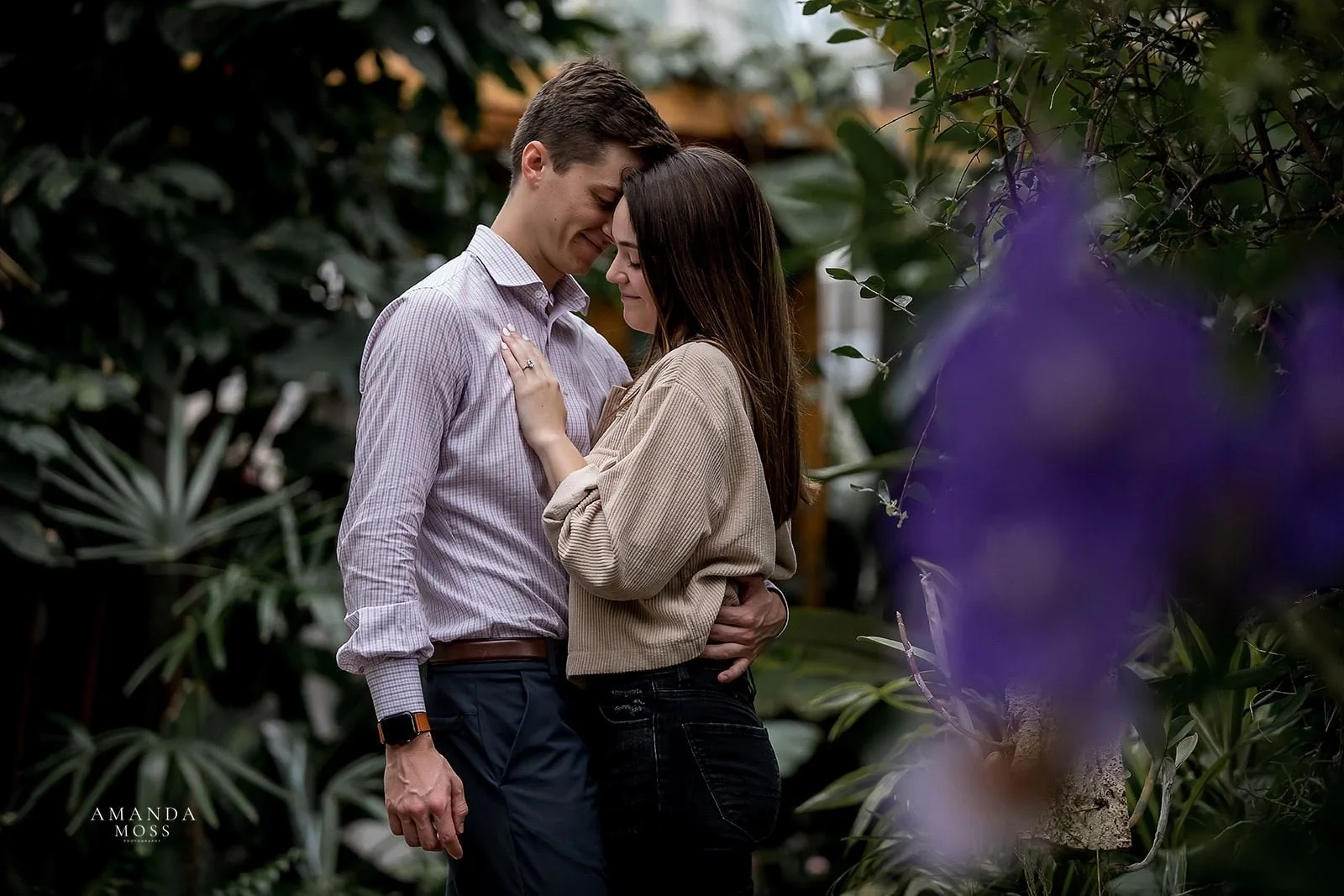 couple embraces while woman admires her new engagement ring in the orchid conservatory at stowe conservancy