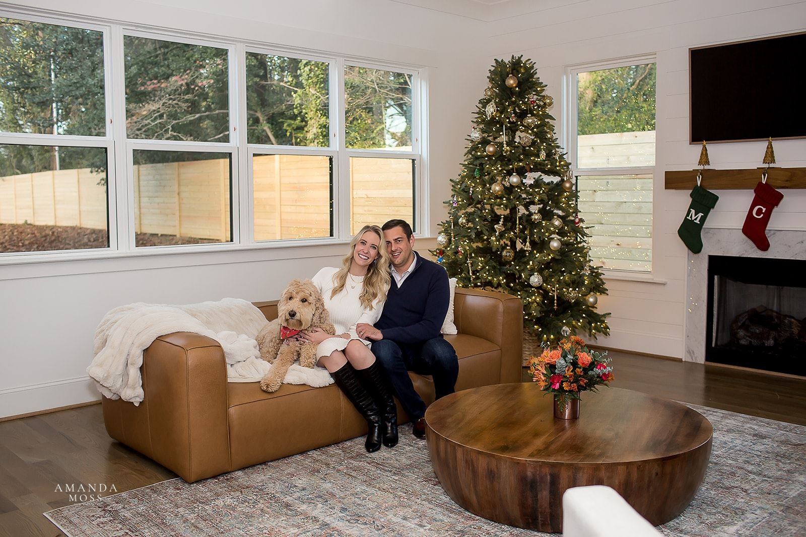 couple and their labradoodle pose on couch in front of decorated christmas tree in their brand new home