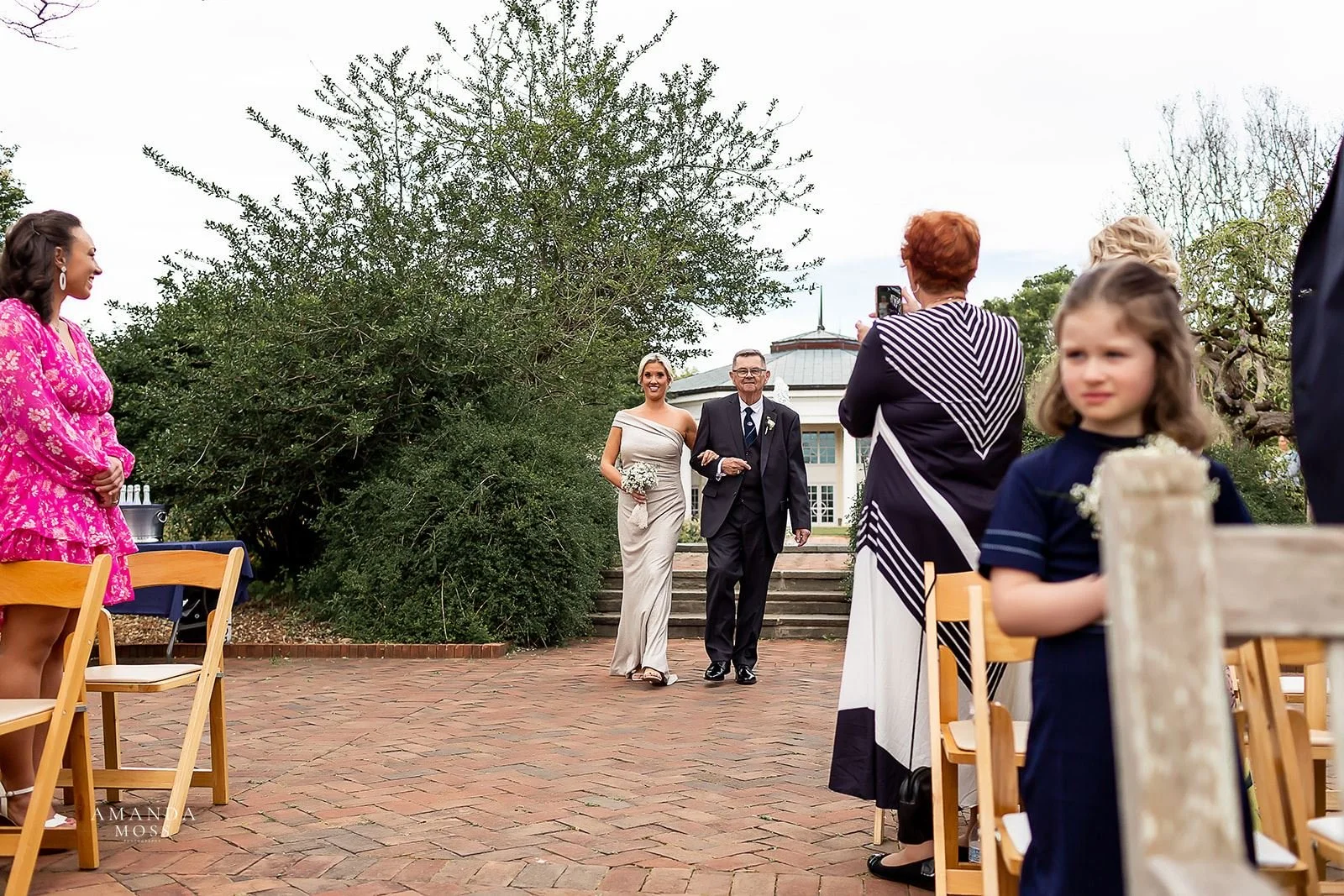 bride walks down the aisle with her father during outdoor wedding at stowe conservancy botanical garden in belmont nc