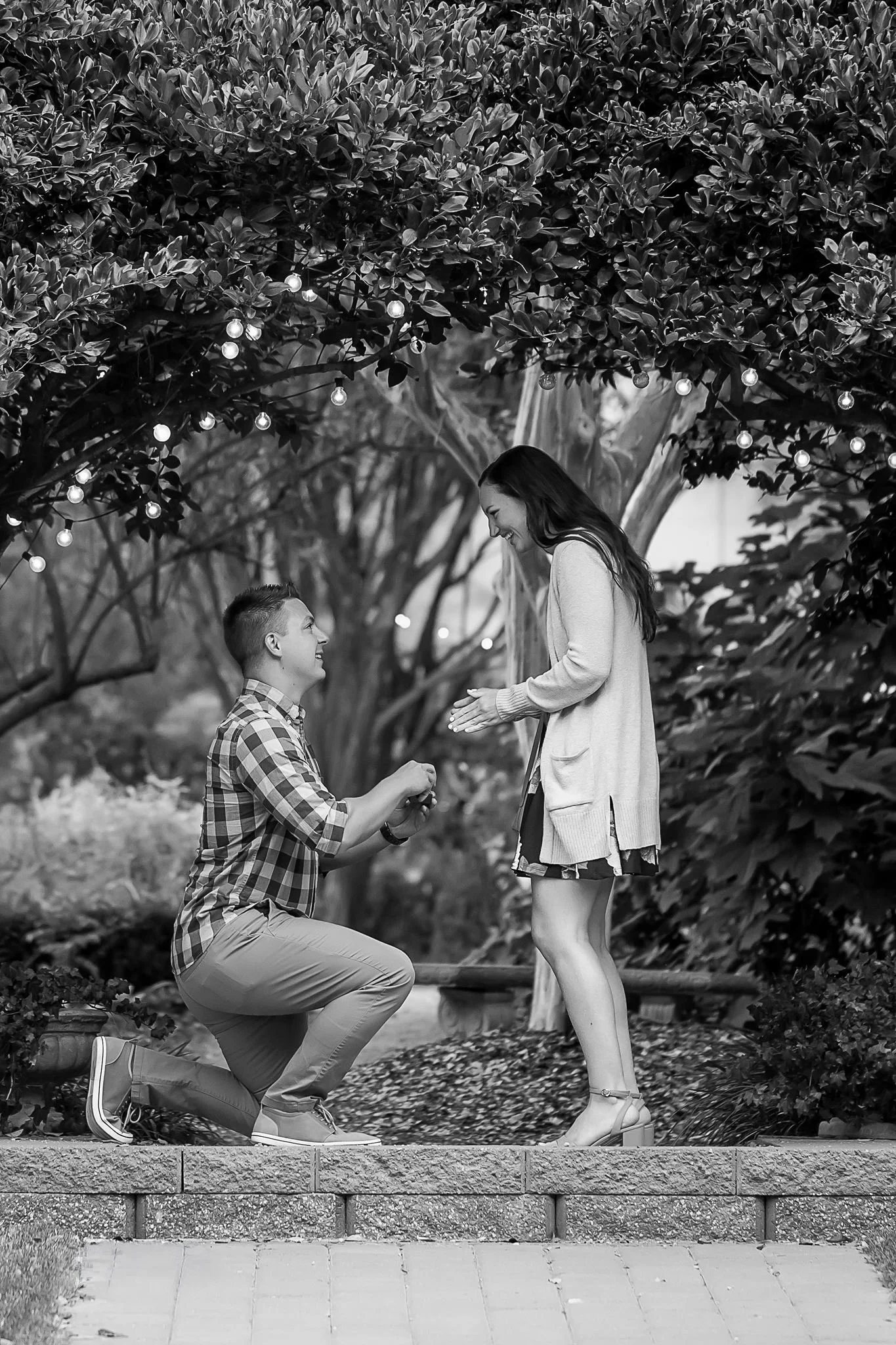 black and white photo of young man on knee proposing to very happy girlfriend