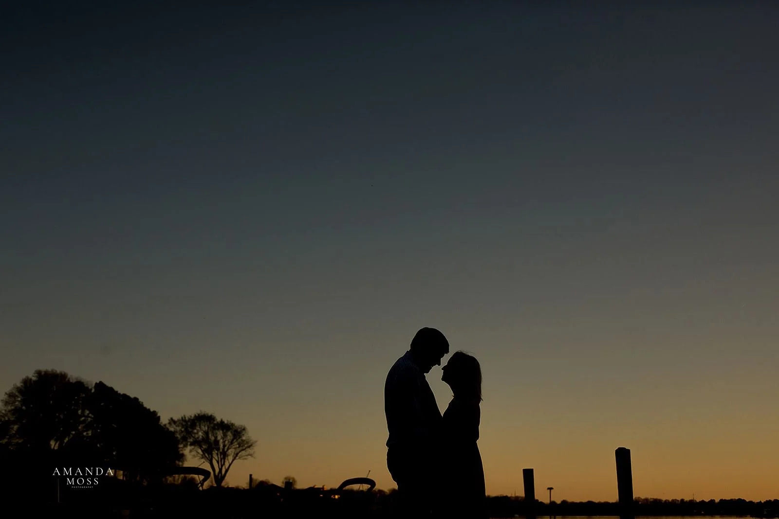 silhoutte photo of couple embracing with big wide sunset behind them at outdoor engagement session at lake norman