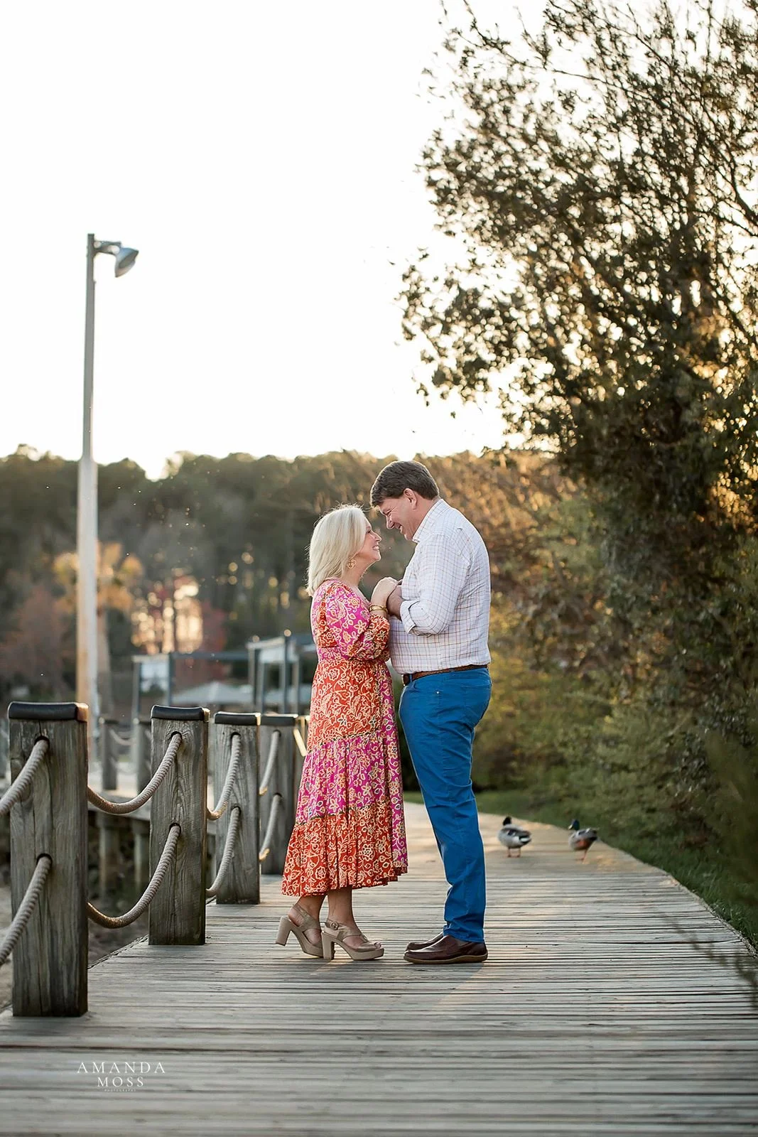 mature couple holds hands and faces each other with big smiles during outdoor engagement session at lake norman
