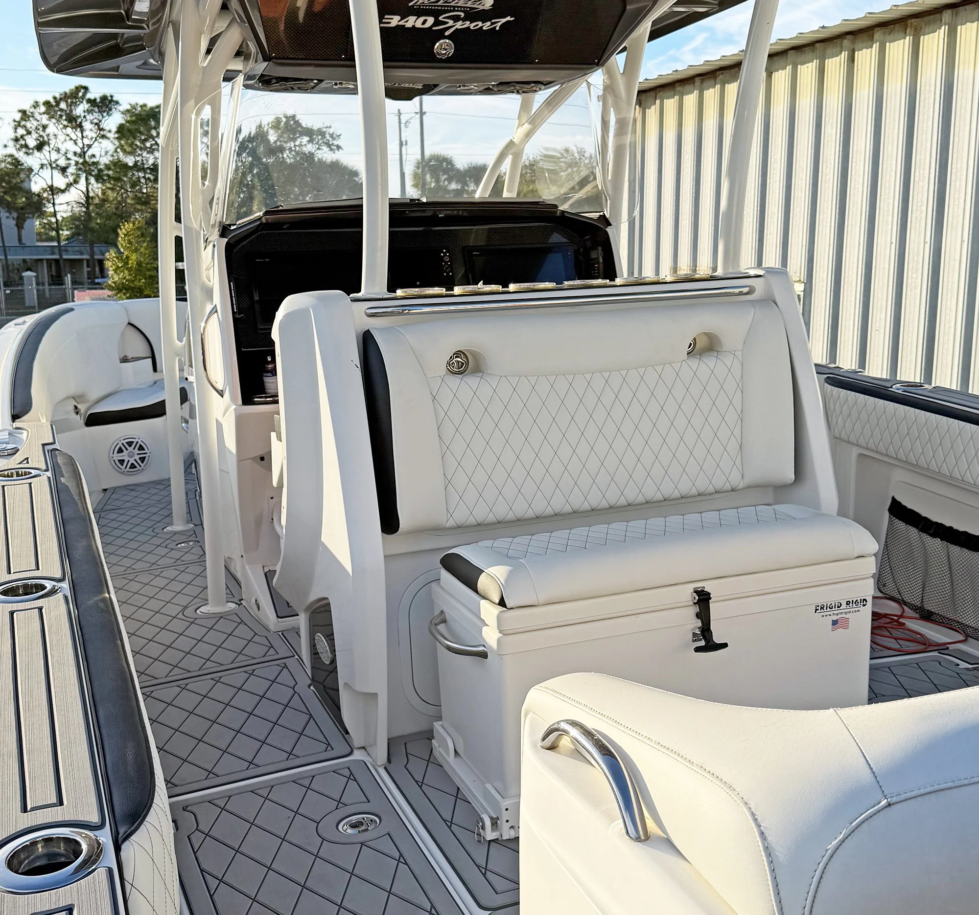 Interior of a white boat with seating and a control panel, featuring a black dashboard and electronic displays, with a patterned floor and a storage compartment in the corner.