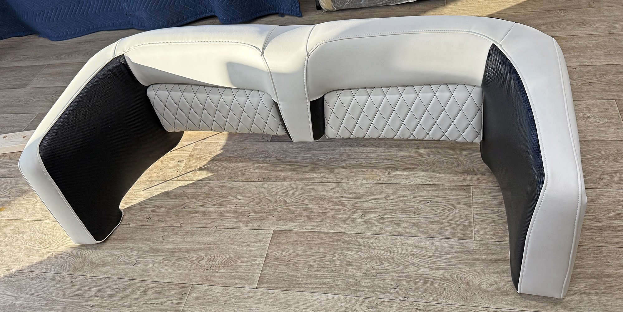 A curved piece of white and black upholstered furniture with diamond-patterned stitching in the center, placed on wooden flooring.