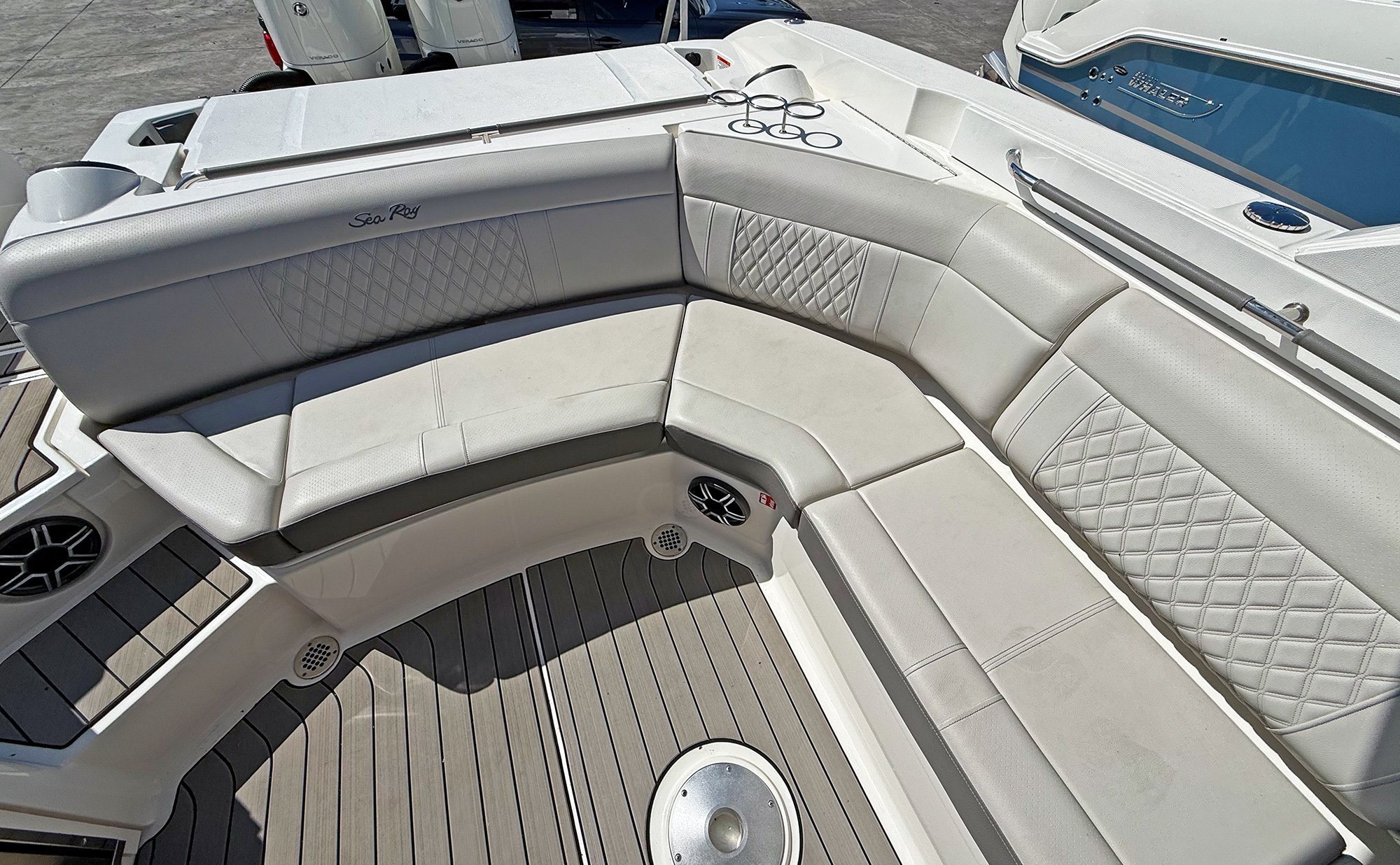 Close-up of the seating area on a boat, with cream-colored cushioned seats with quilted stitching, a rod holder with fishing rods, and a wooden deck with black and tan stripes.