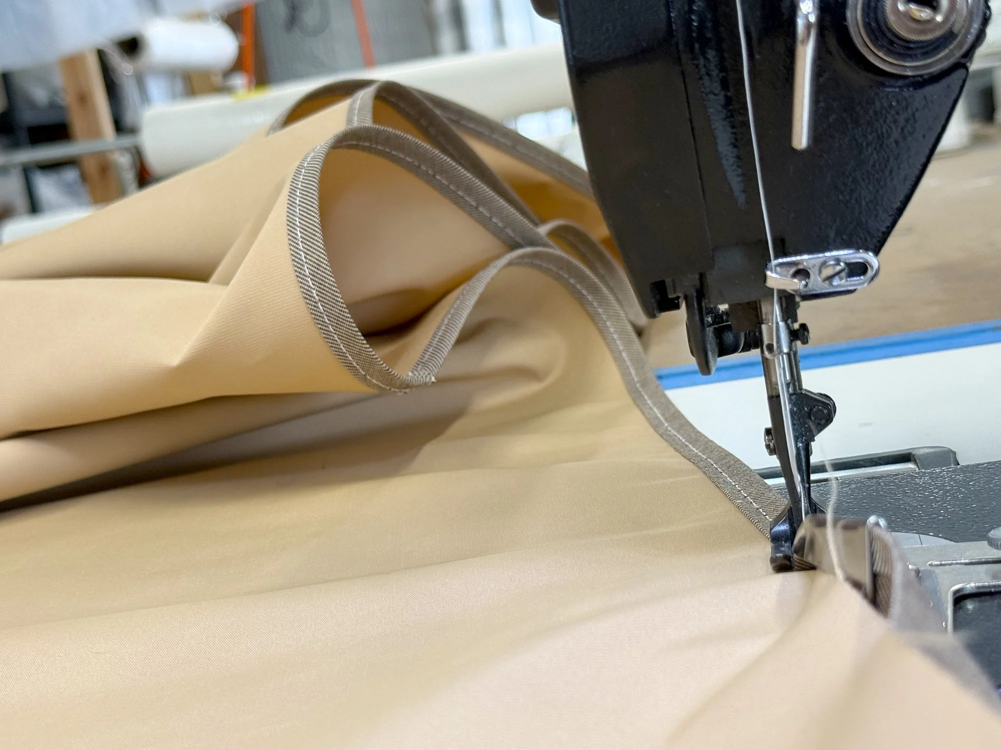 A tan fabric being sewn with beige and gray stitching, under a sewing machine.