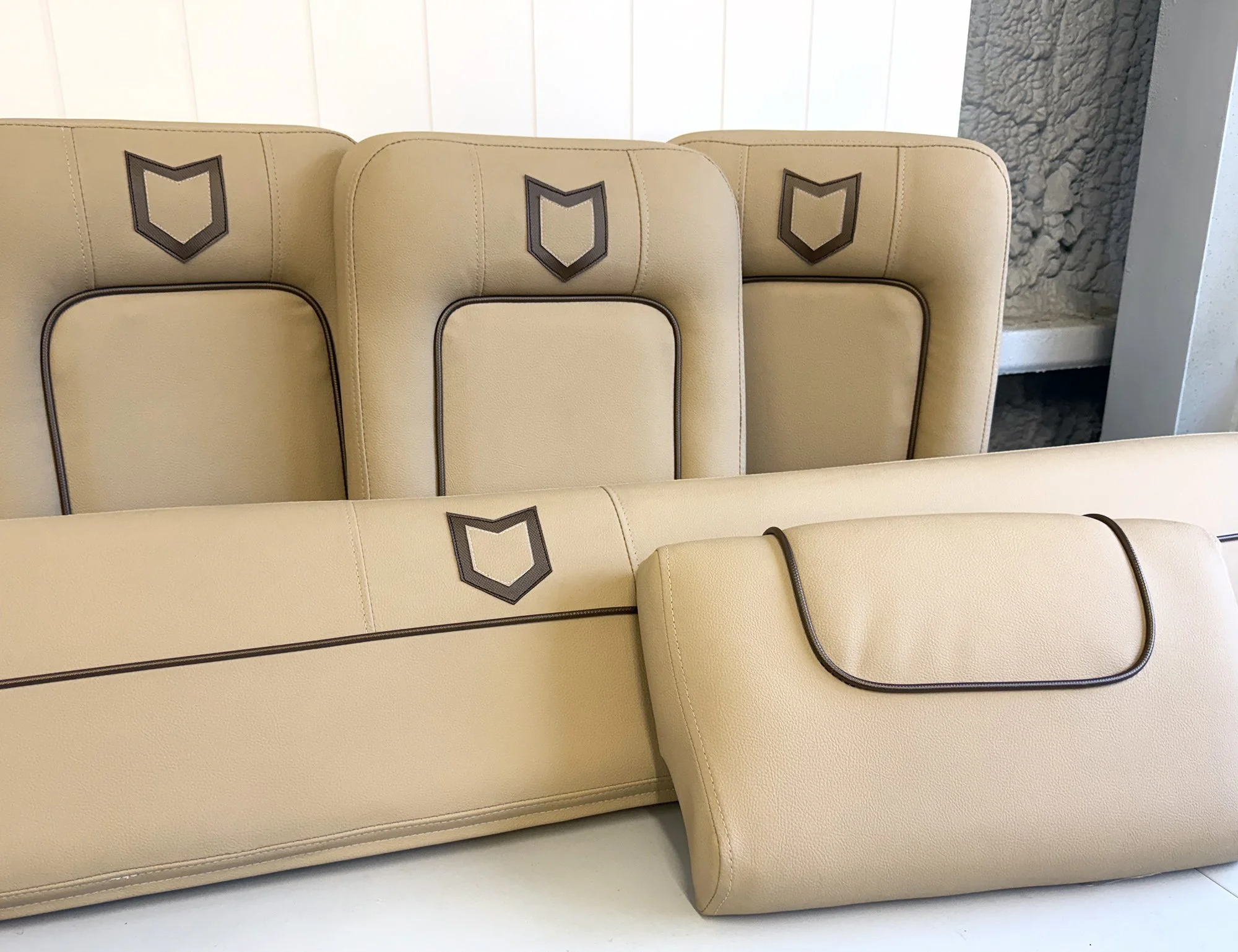 A row of beige retro-style college or stadium seats with dark trim, featuring a shield-shaped emblem on the headrest area.