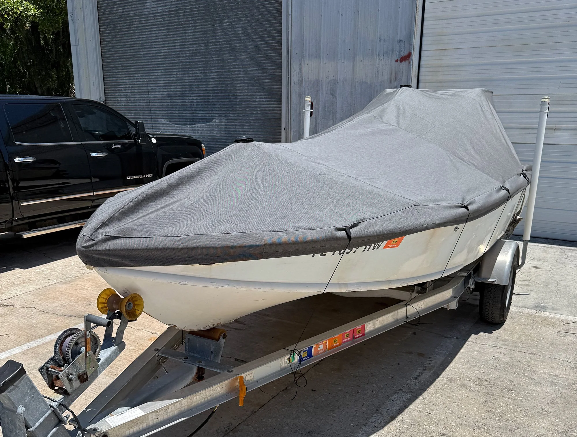 A boat covered with a tarp on a trailer, parked next to a black vehicle and metal storage units.