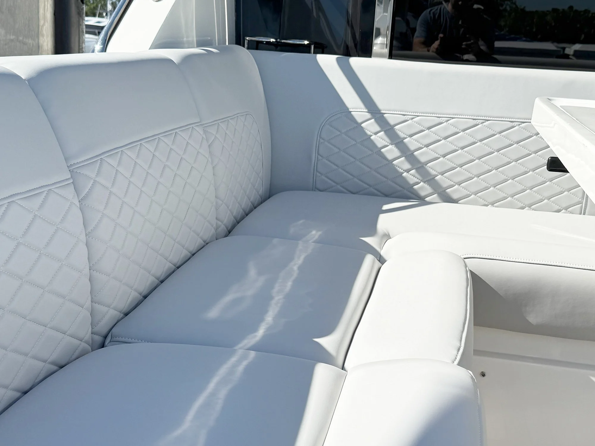 Close-up of the interior of a boat with white cushioned seats featuring diamond-pattern stitching, and sunlight casting shadows on the seats.