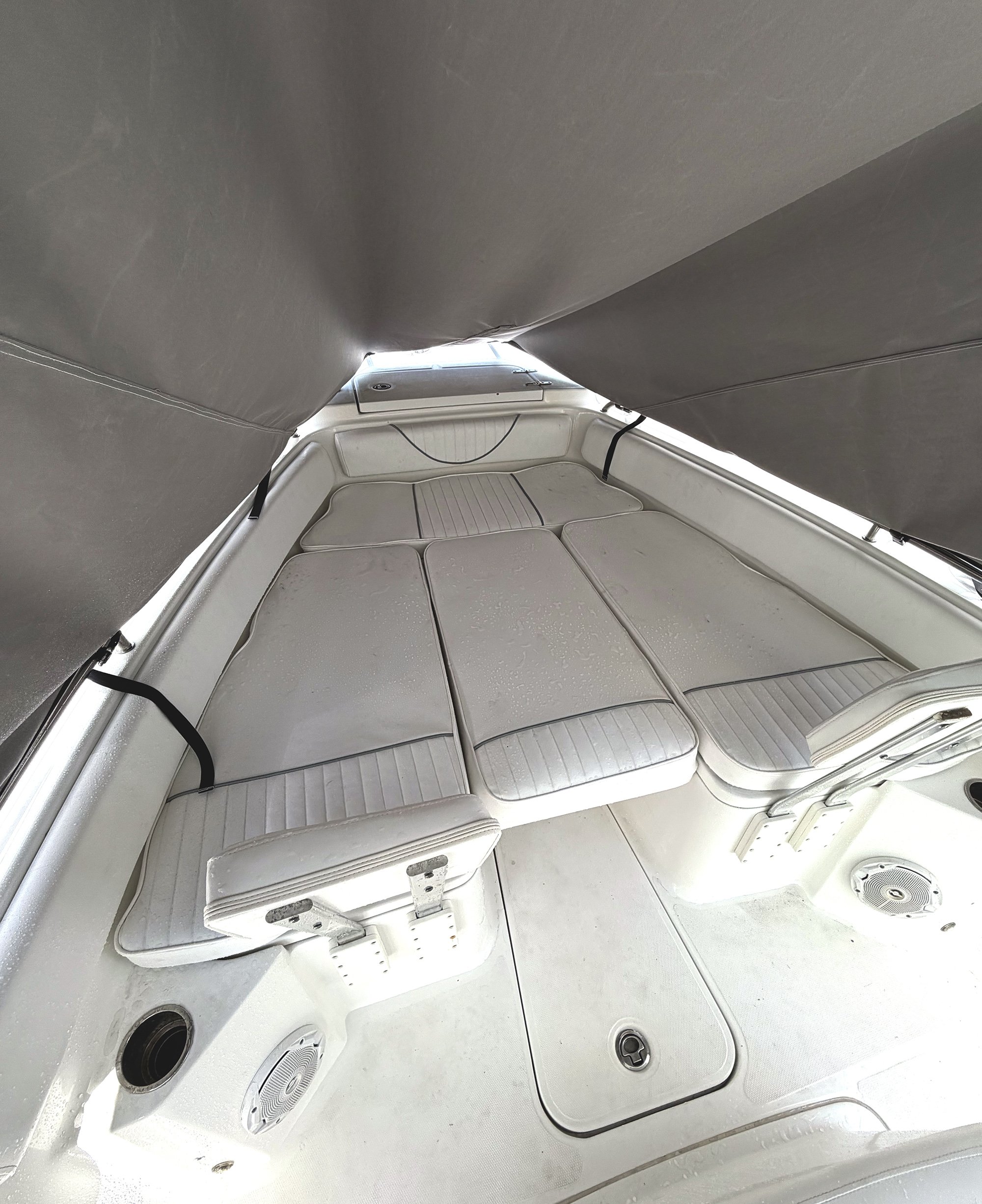 Inside of a boat showing a padded seating area with storage compartments underneath, surrounded by gray canvas curtains, and built-in speakers in the walls.