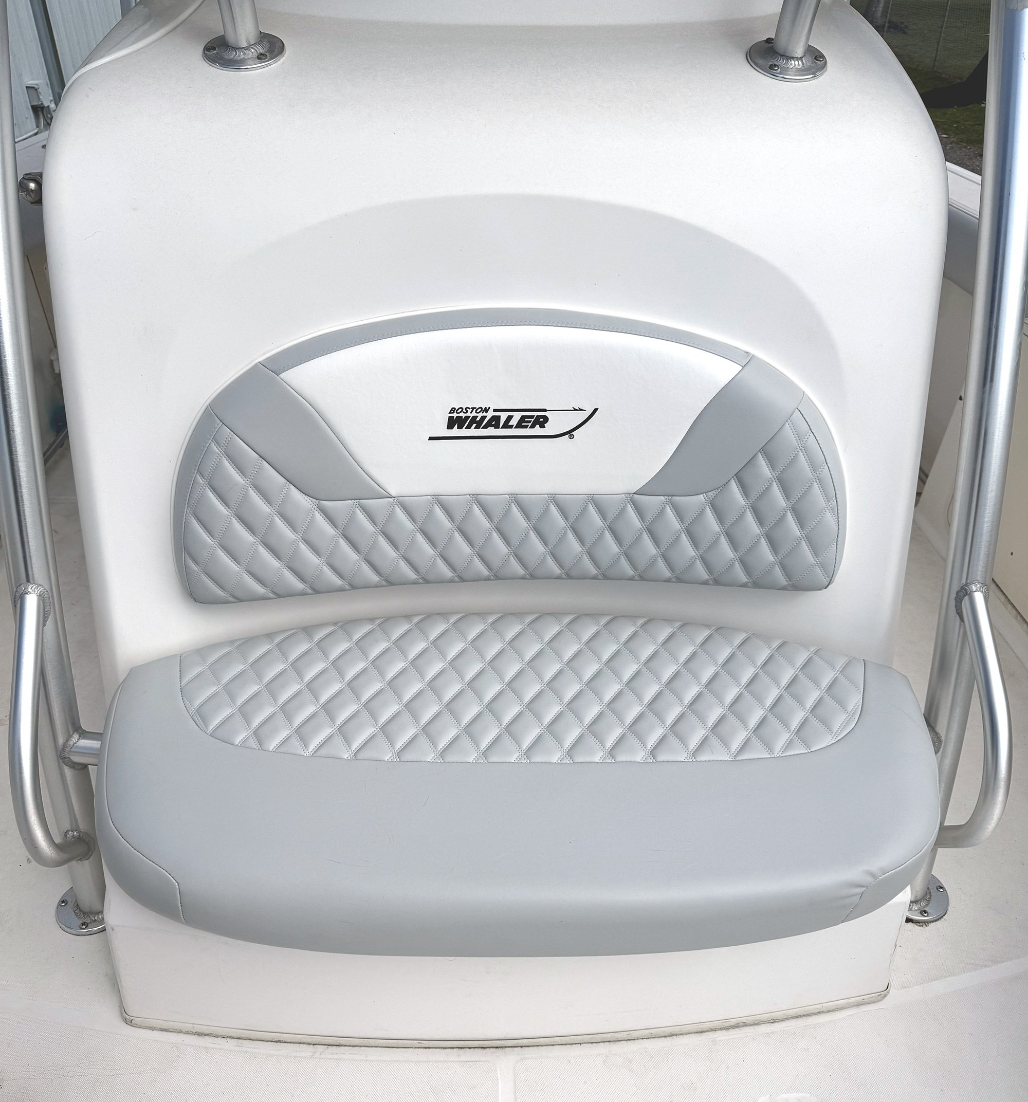 White boat seat with a quilted gray backrest and the logo 'Boston Whaler' in black, parts of the boat's structure and metal supports surrounding it.