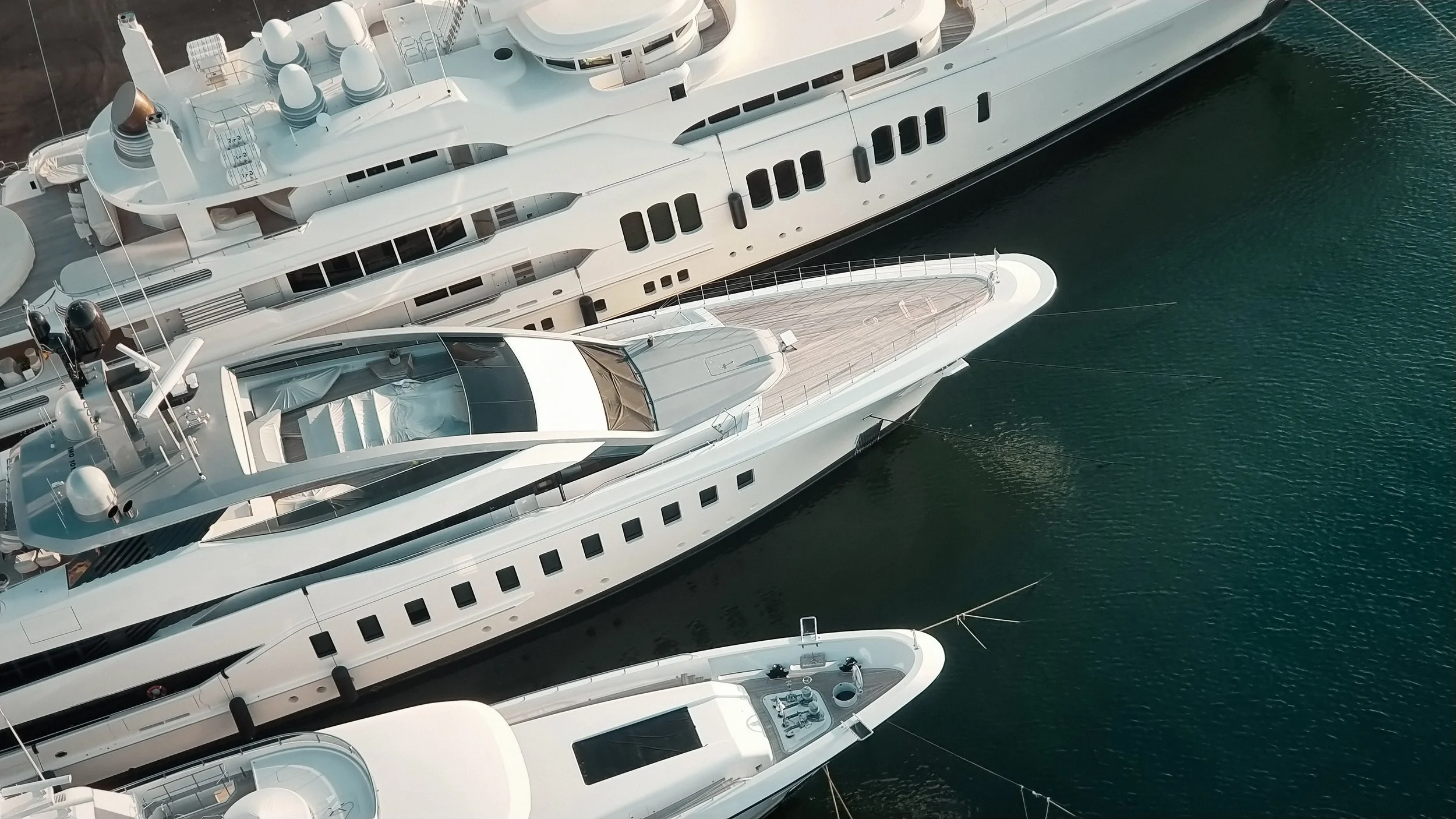 Aerial view of multiple large white yachts docked in a marina.