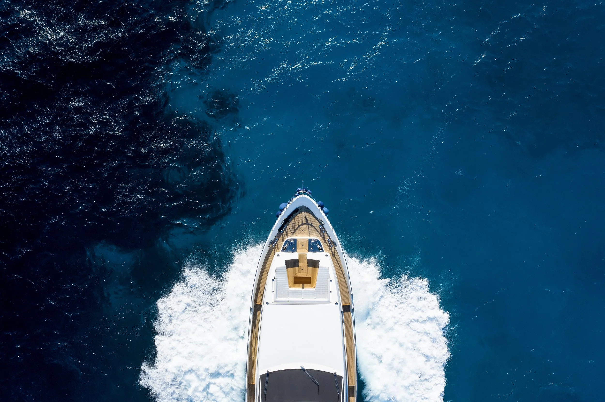 An aerial view of a yacht's bow cutting through deep blue ocean water.