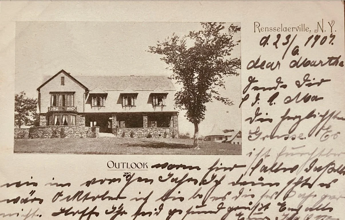 A sepia-toned photograph of a large, two-story house with porch and dormer windows, surrounded by grass and trees, with handwritten notes on the right side and the word "OUTLOOK" printed at the bottom.