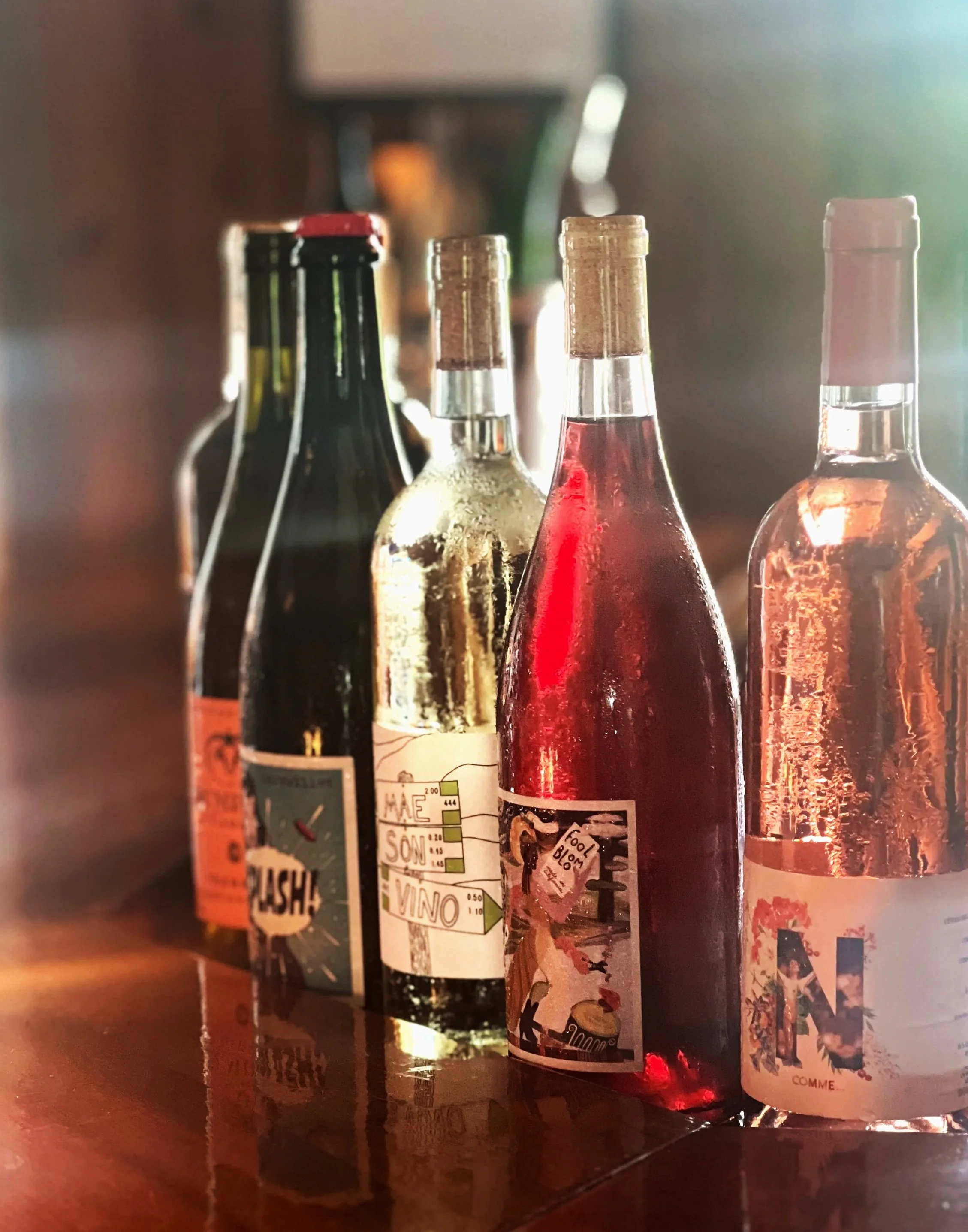 Close-up of several glass bottles with different labels, some are partially visible, placed on a wooden surface with warm lighting.