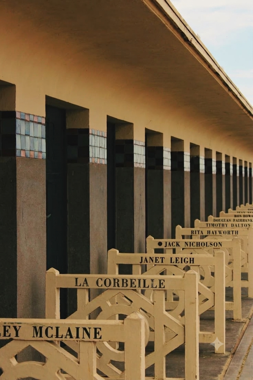 Rows of beige benches with black engraved names in front of a wall with small windows and a beige roof, outdoor setting.