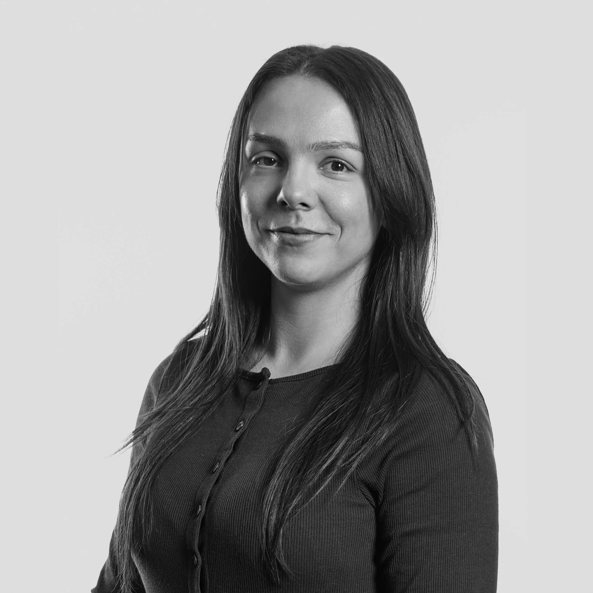 Black and white portrait of Amber Dewick with long straight hair, smiling gently, against a plain light background.