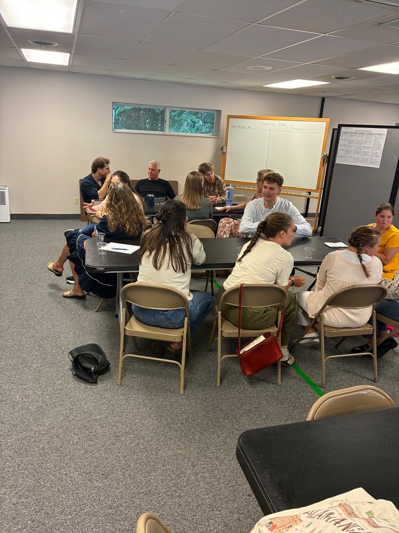 Students sitting at tables in a classroom with a whiteboard that says 'Lektion 10' and 'Hottest Day Jesus'.